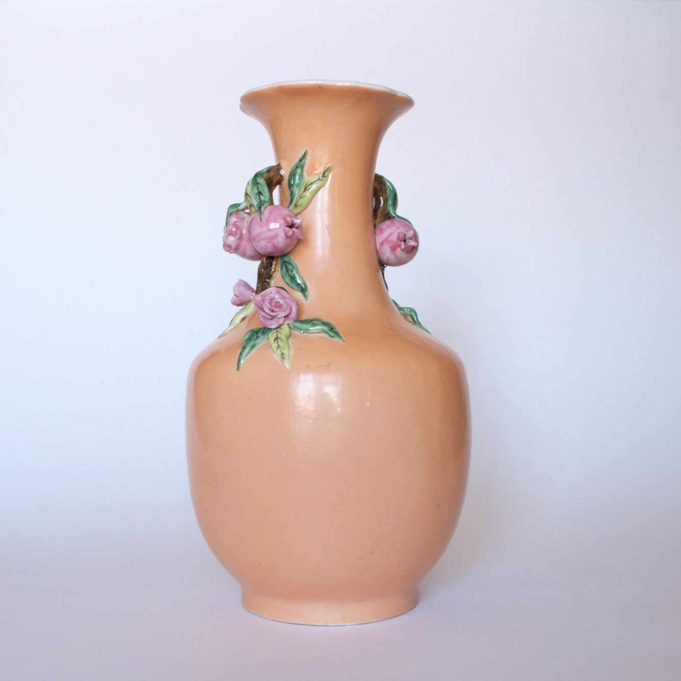 The Euro Trash Vintage Hand-Painted Floral Ceramic Vase features a glossy peach finish with raised pink flowers and green leaves on its narrow neck, displayed against a plain white background.