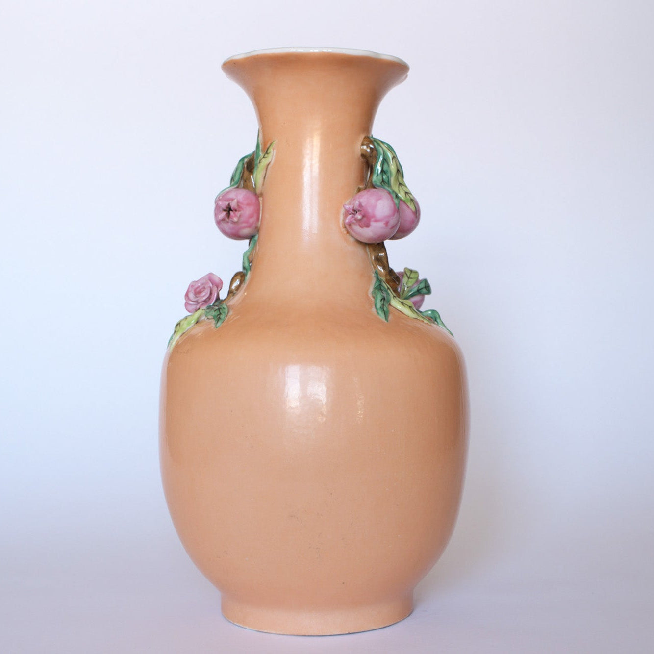 The Euro Trash Vintage Hand-Painted Floral Ceramic Vase features a glossy peach finish, narrow neck, pink sculpted flowers, and green leaves, displayed against a plain light background.
