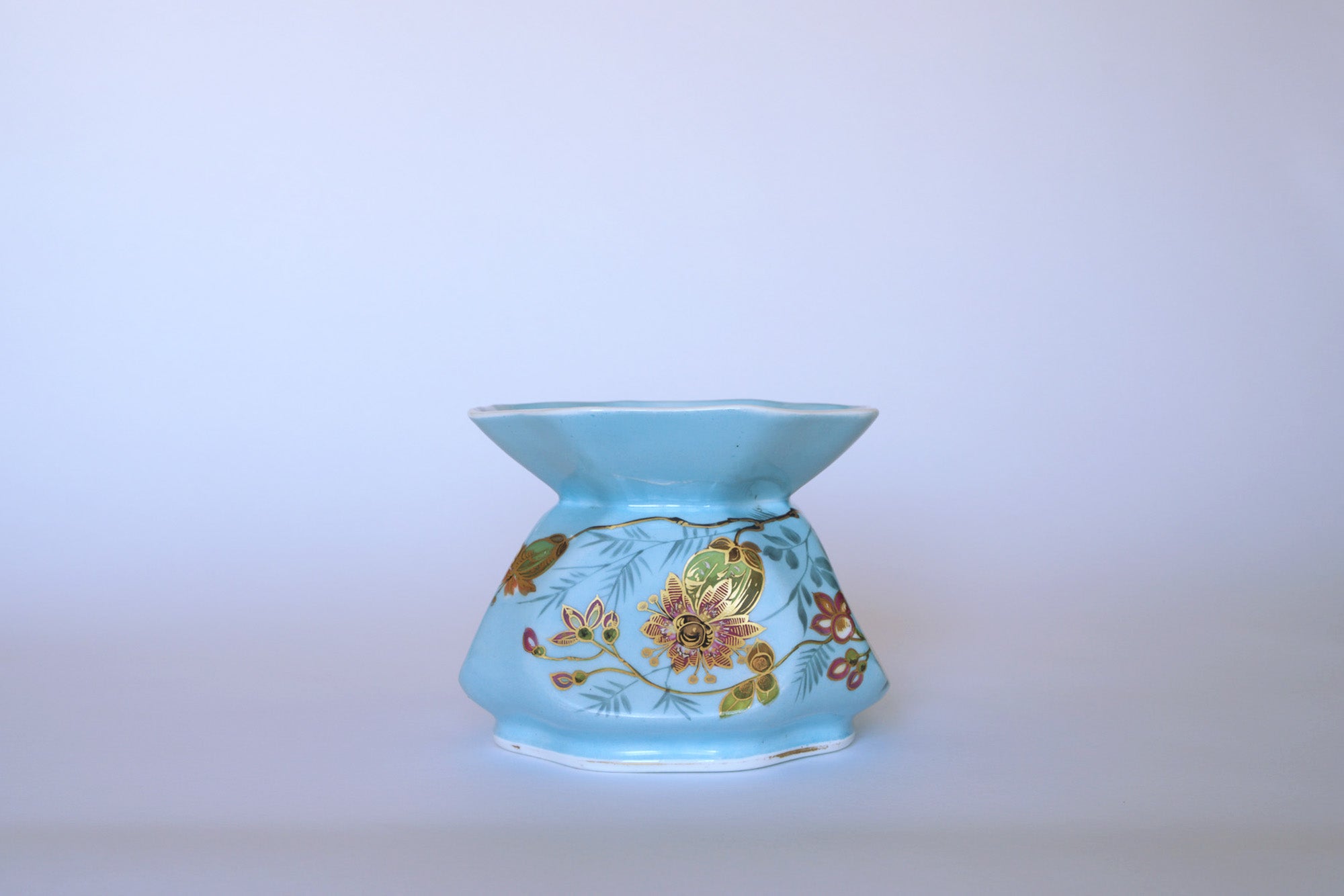 The Euro Trash Vintage Blue Floral Porcelain Vase features a light blue finish, wide flared rim, narrow base, and gold and red hand-painted floral designs, shown against a plain light background.