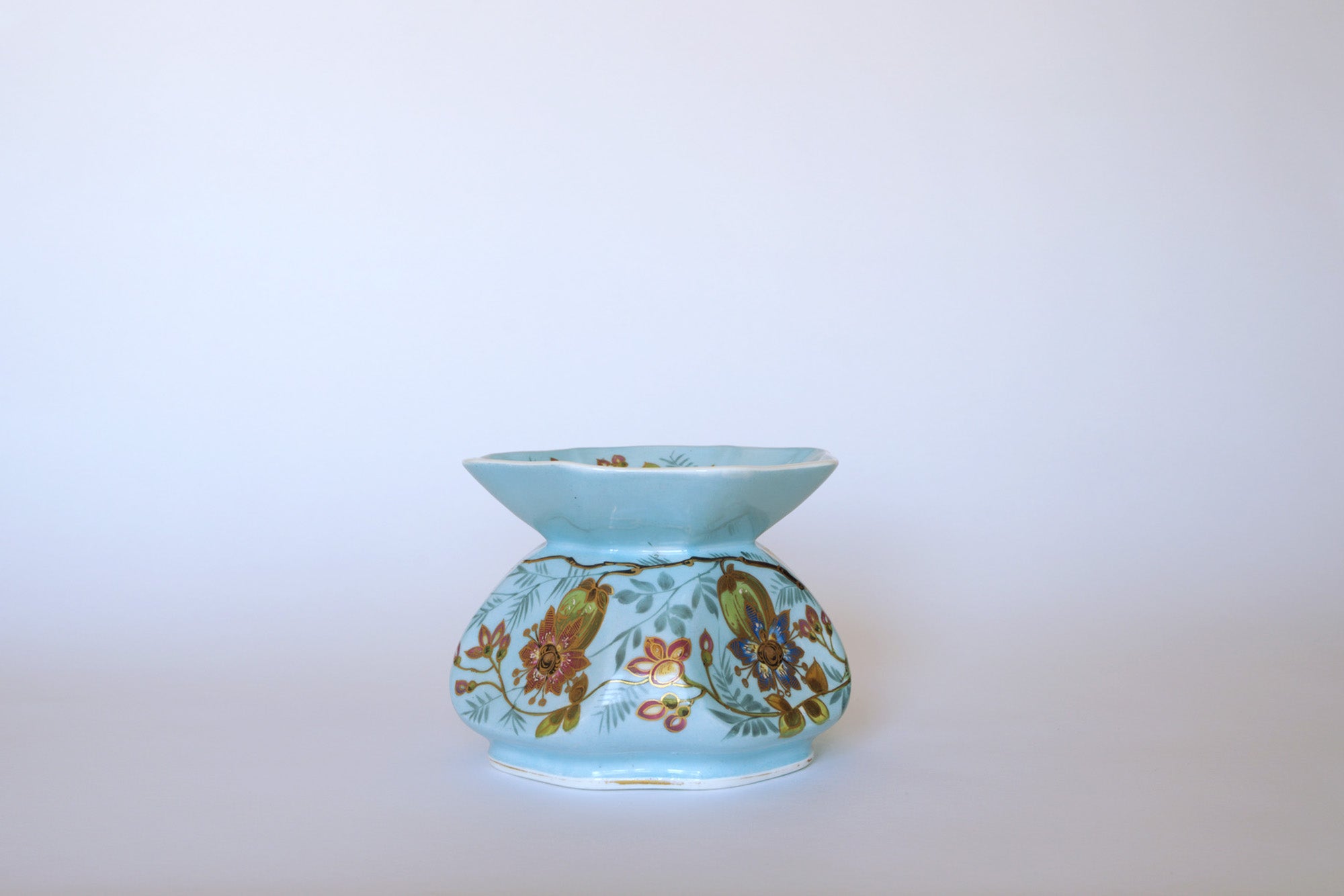 The Vintage Blue Floral Porcelain Vase by Euro Trash features a light blue finish, wide flared rim, and hand-painted red, yellow, and green floral designs, displayed against a plain white background.