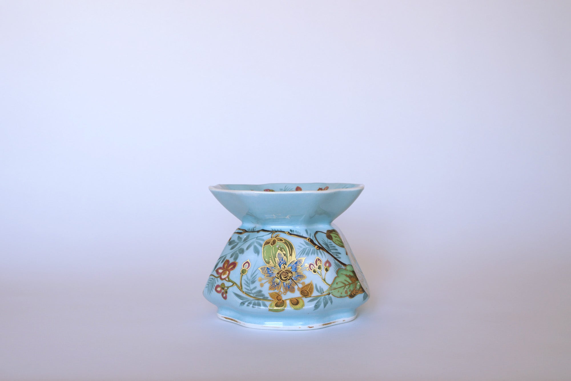 The Euro Trash Vintage Blue Floral Porcelain Vase features a light blue glaze, wide flared top, and hand-painted green, yellow, and red floral designs—all set against a plain white background.