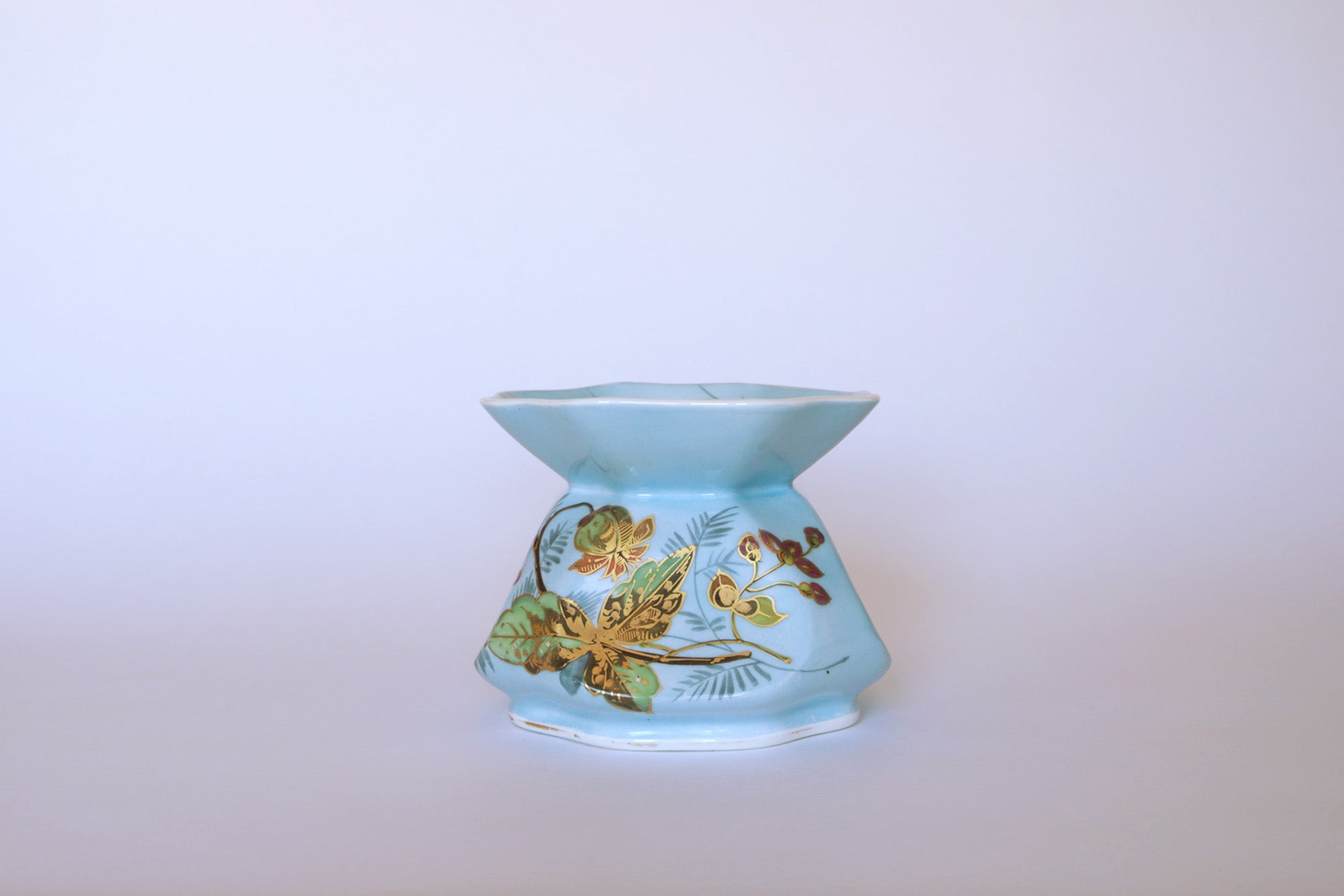 The Euro Trash Vintage Blue Floral Porcelain Vase features a light blue hue, flared rim, and hand-painted gold and brown leaf designs, shown on a plain white background.