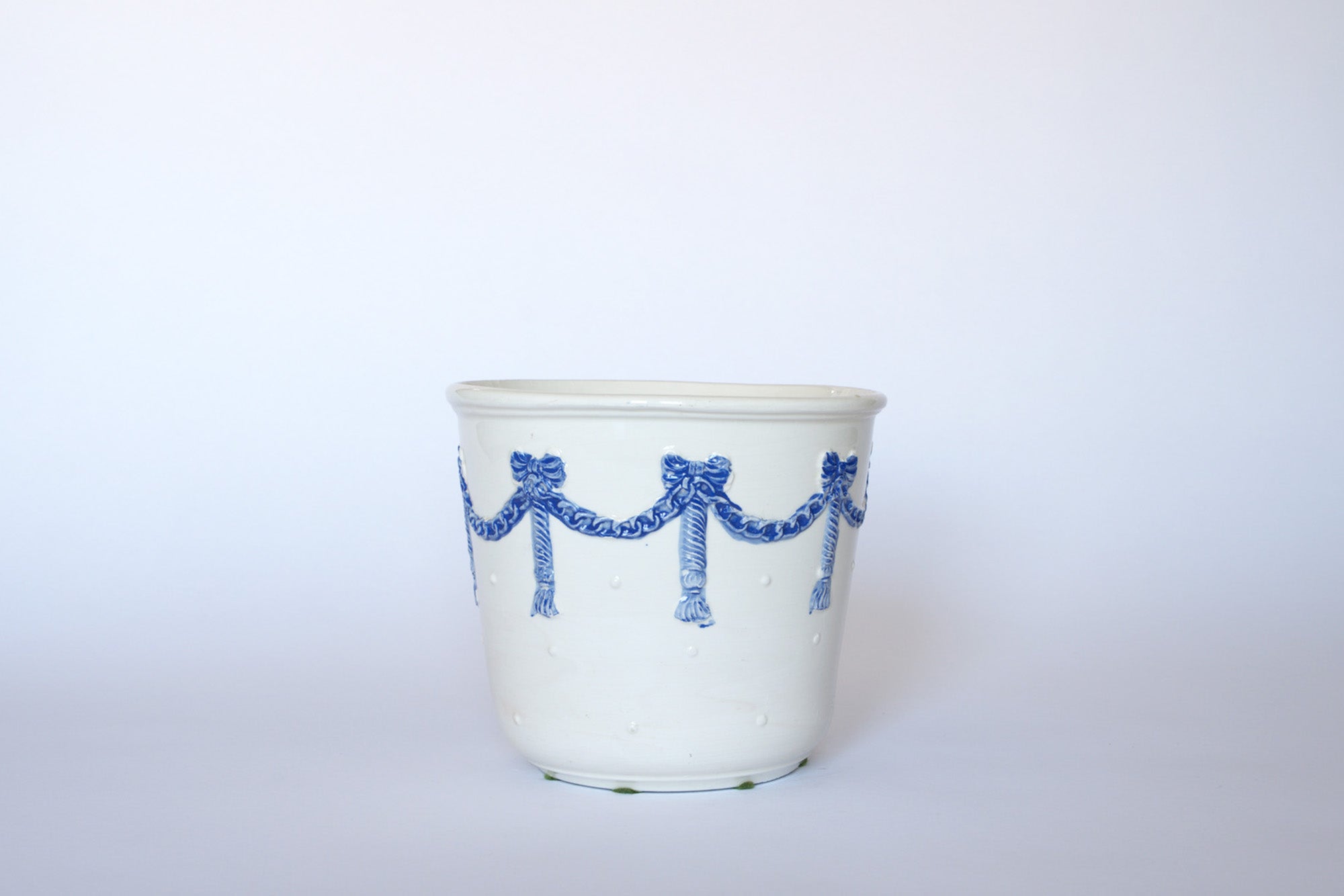 The Euro Trash Vintage White & Blue Ribbon Ceramic Cachepot features blue ribbon garlands and raised dots on white ceramic, evoking classic vintage style.
