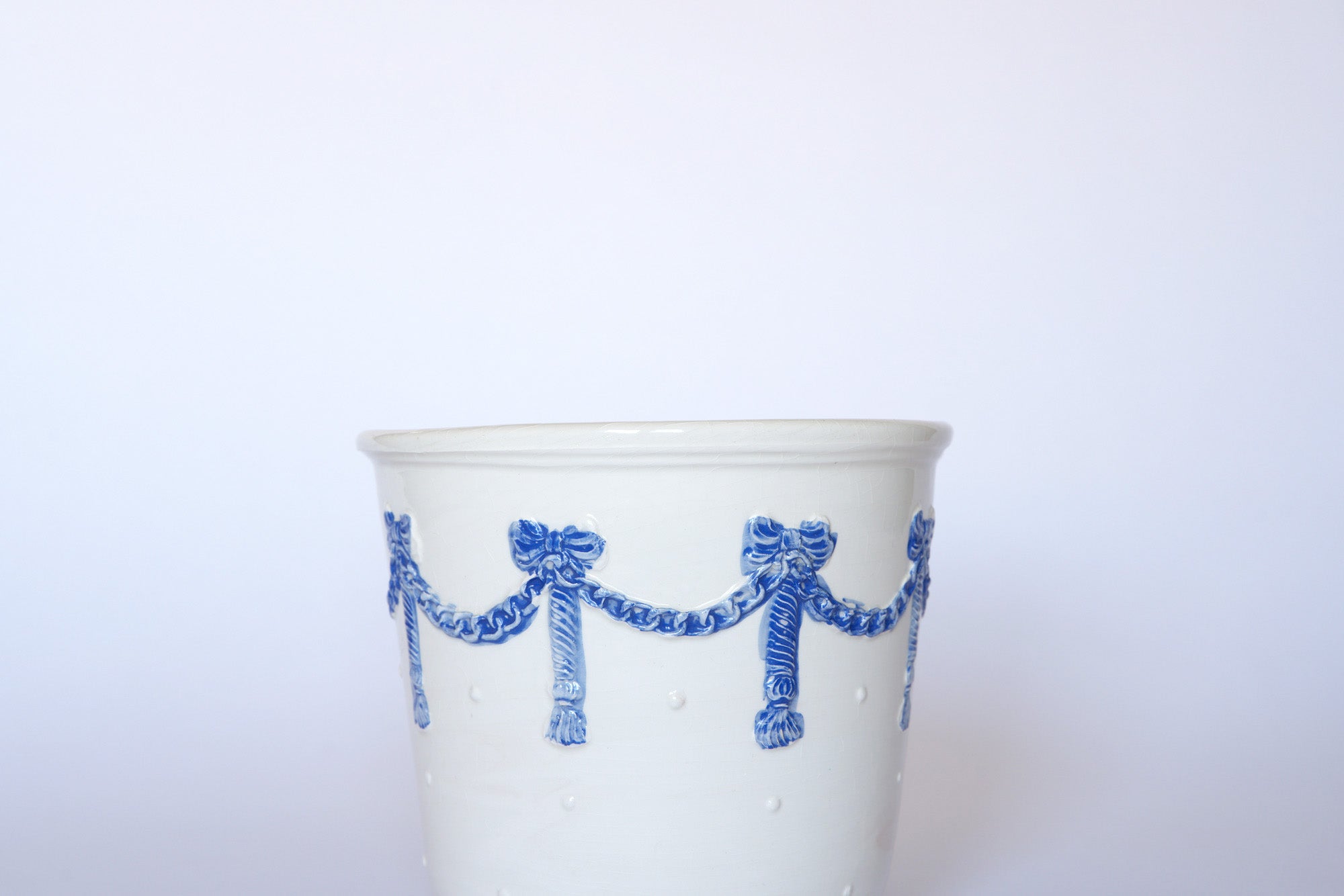 The Euro Trash Vintage White & Blue Ribbon Ceramic Cachepot features a blue garland and bow motif near the rim—ideal for European-inspired decor. Shown against a plain white background.