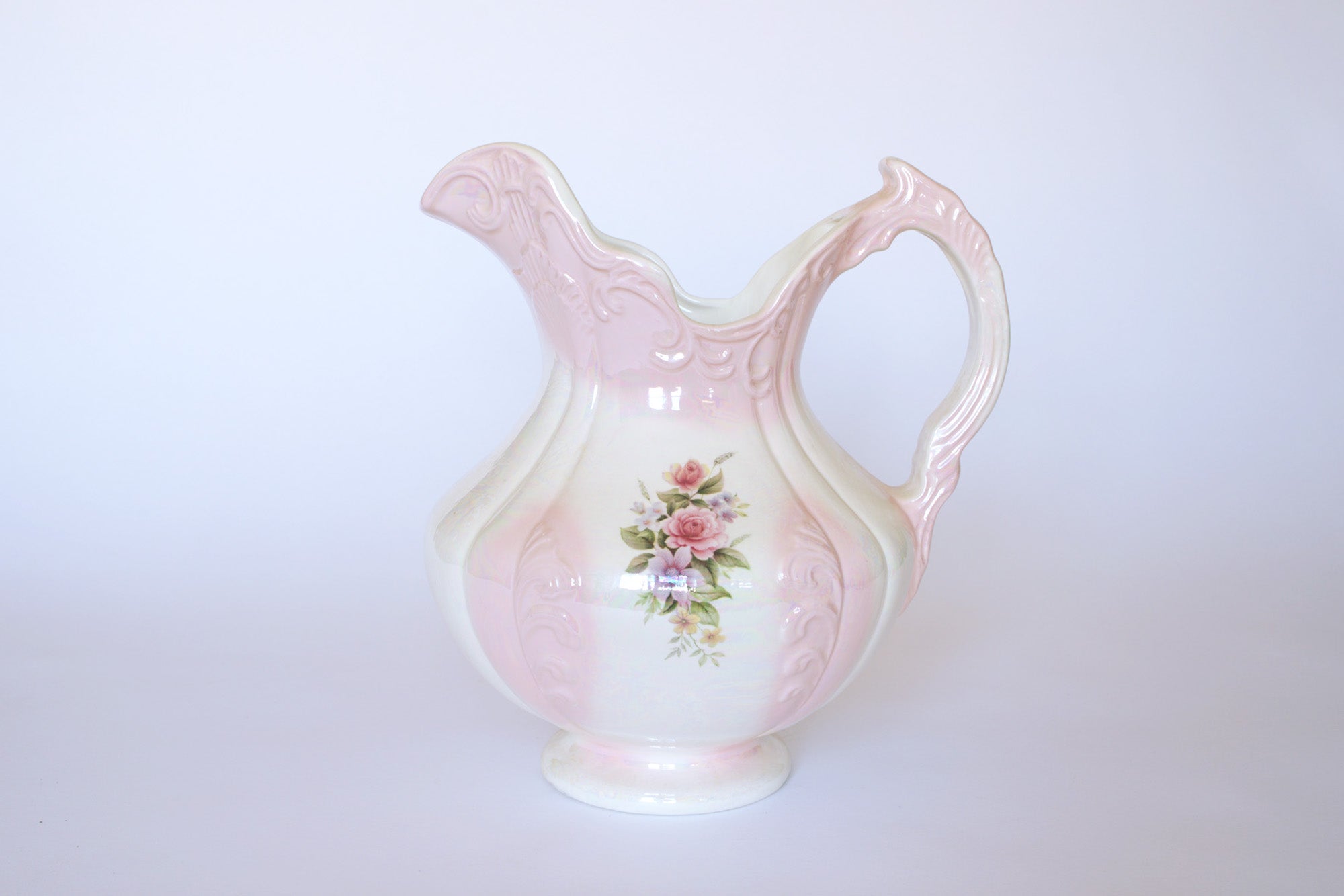The Euro Trash Vintage Pink Lustreware Floral Ceramic Pitcher features a curved handle, ornate details, and hand-painted pink roses on a white background.