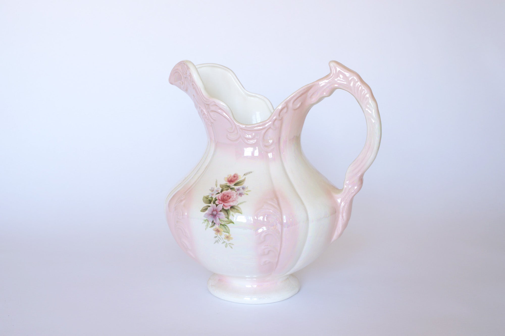 The Euro Trash Vintage Pink Lustreware Floral Ceramic Pitcher features a hand-painted pink rose design, ornate handle, and glossy pink glaze, shown against a plain white background.