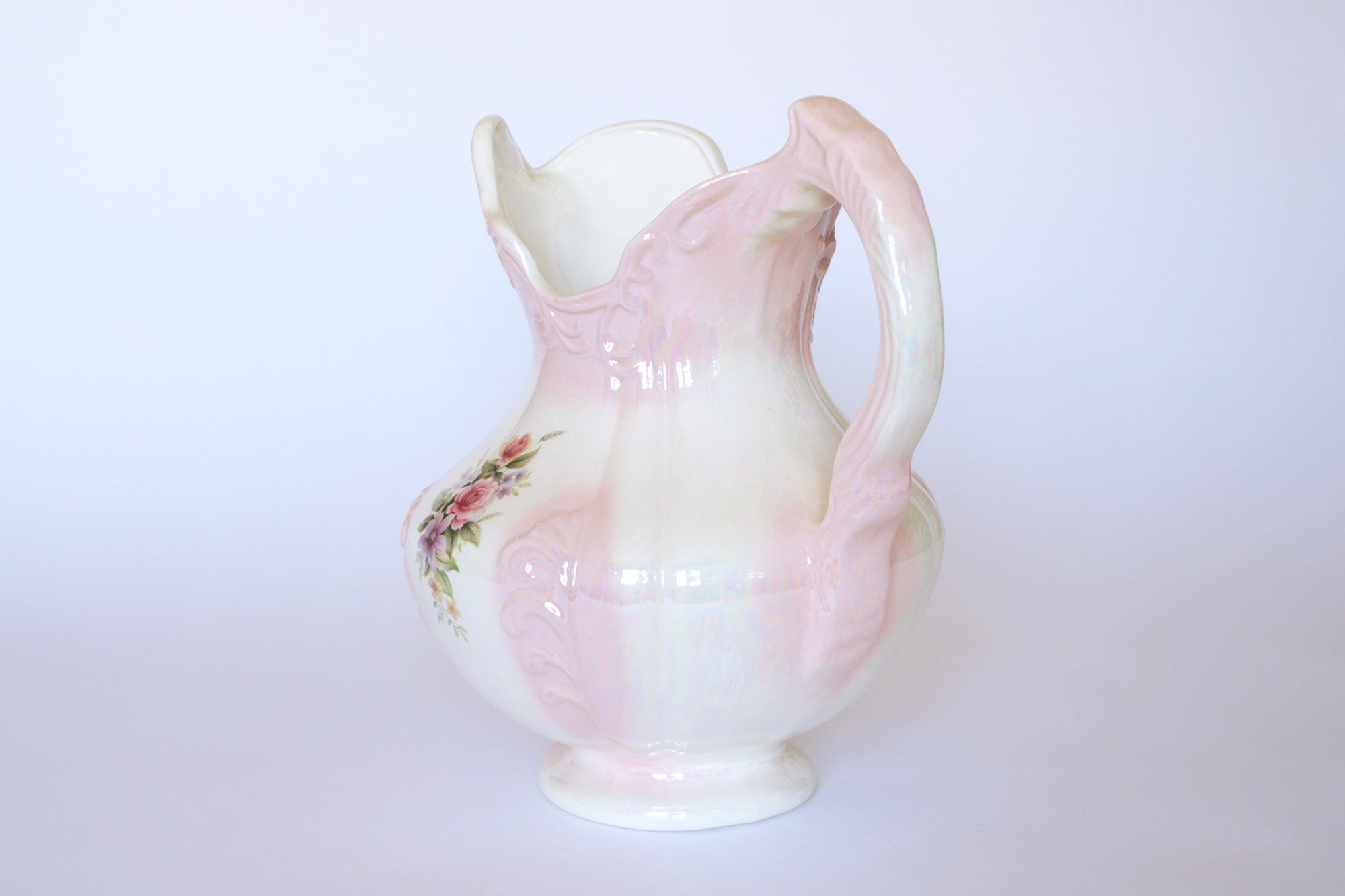The Euro Trash Vintage Pink Lustreware Floral Ceramic Pitcher features a large ornate handle, hand-painted flowers, and a lustrous pink glaze on white ceramic.