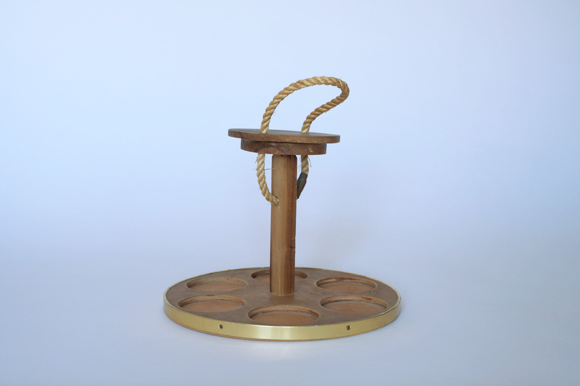 The Euro Trash Vintage Wooden Cupholder features six circular slots, a rope handle, and a brass-trimmed round base, adding minimalist wood decor charm against a plain white background.