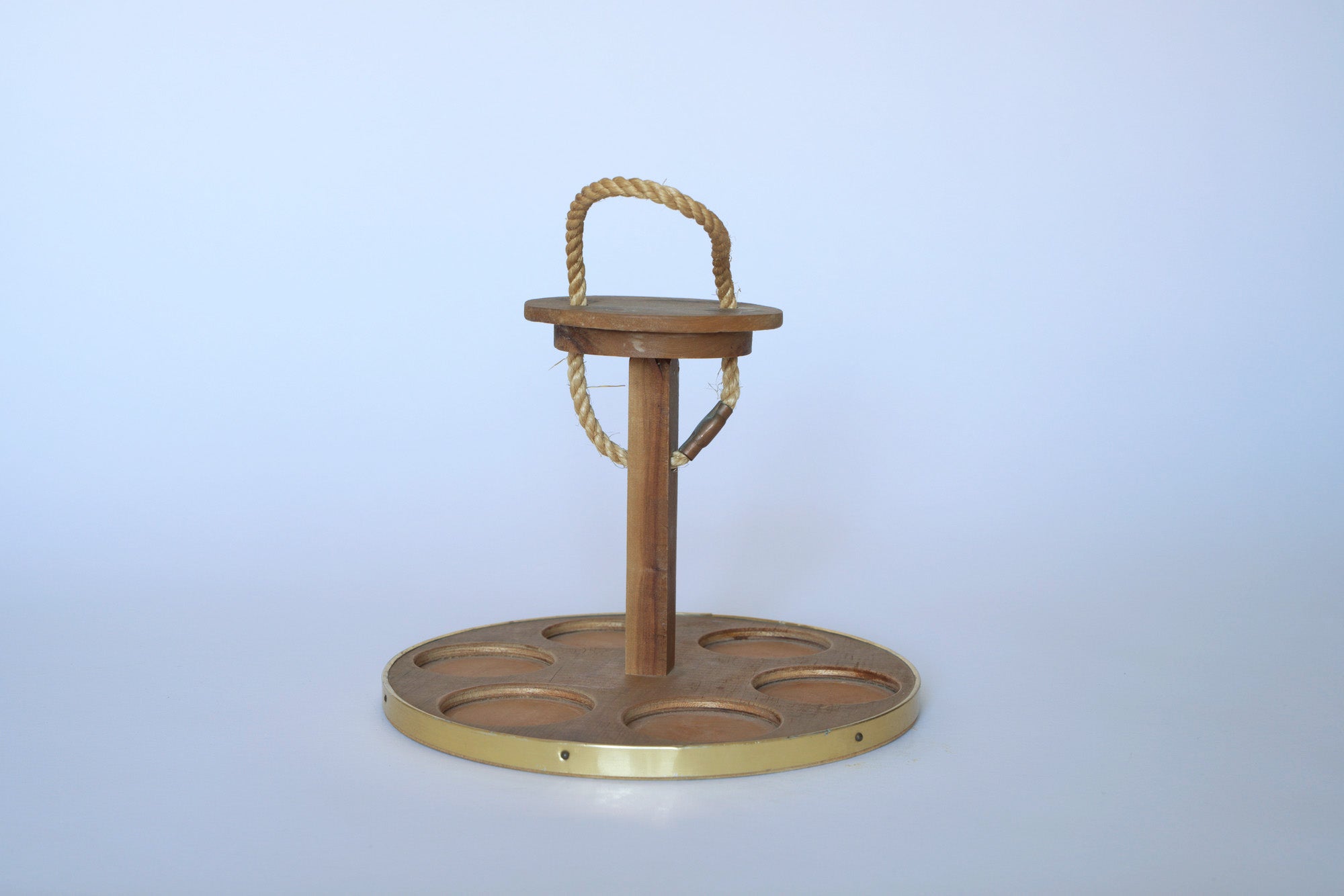 The Euro Trash Vintage Wooden Cupholder features six circular slots, a central pole, brass accents, and a rope handle—ideal as minimal wood decor on a plain light background.