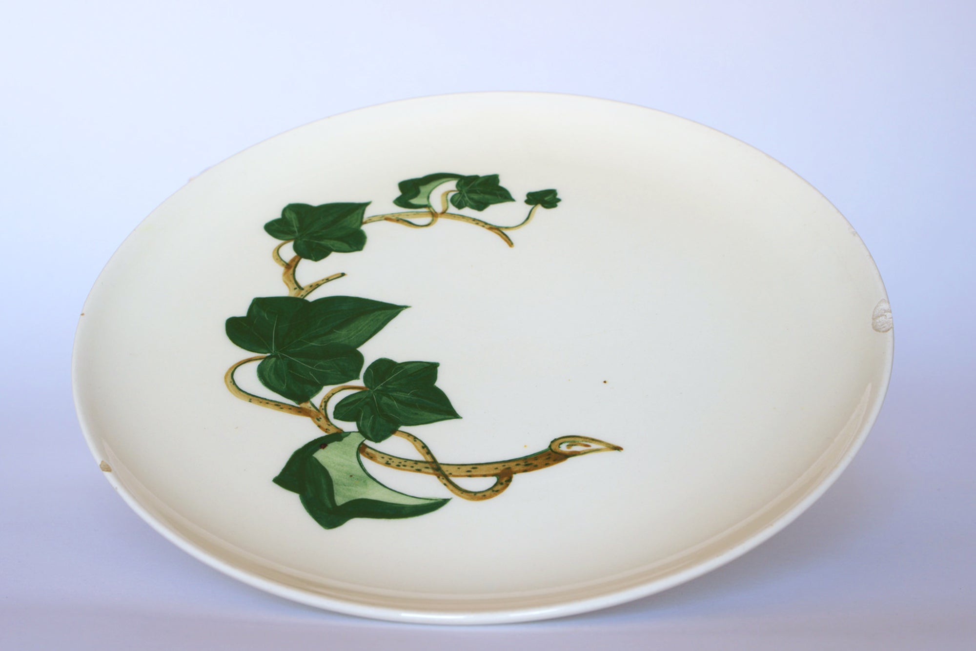 The Vintage Ivory Ceramic Bowl with Ivy Leaf by Euro Trash features hand-painted green ivy vines on a white rim, making it a charming decorative centerpiece for any table.