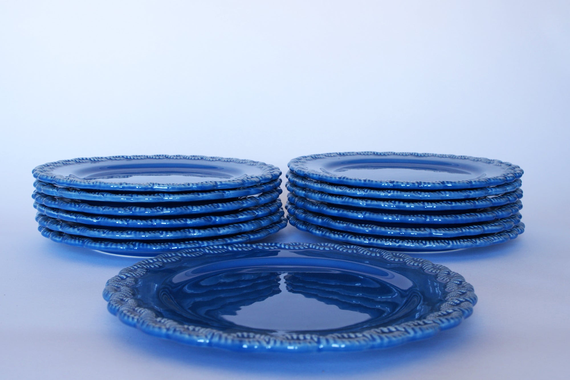 A set of thirteen Euro Trash Vintage Blue Rim Dinner Plates with beaded edges is stacked in two piles, with one plate placed separately in front on a white background.
