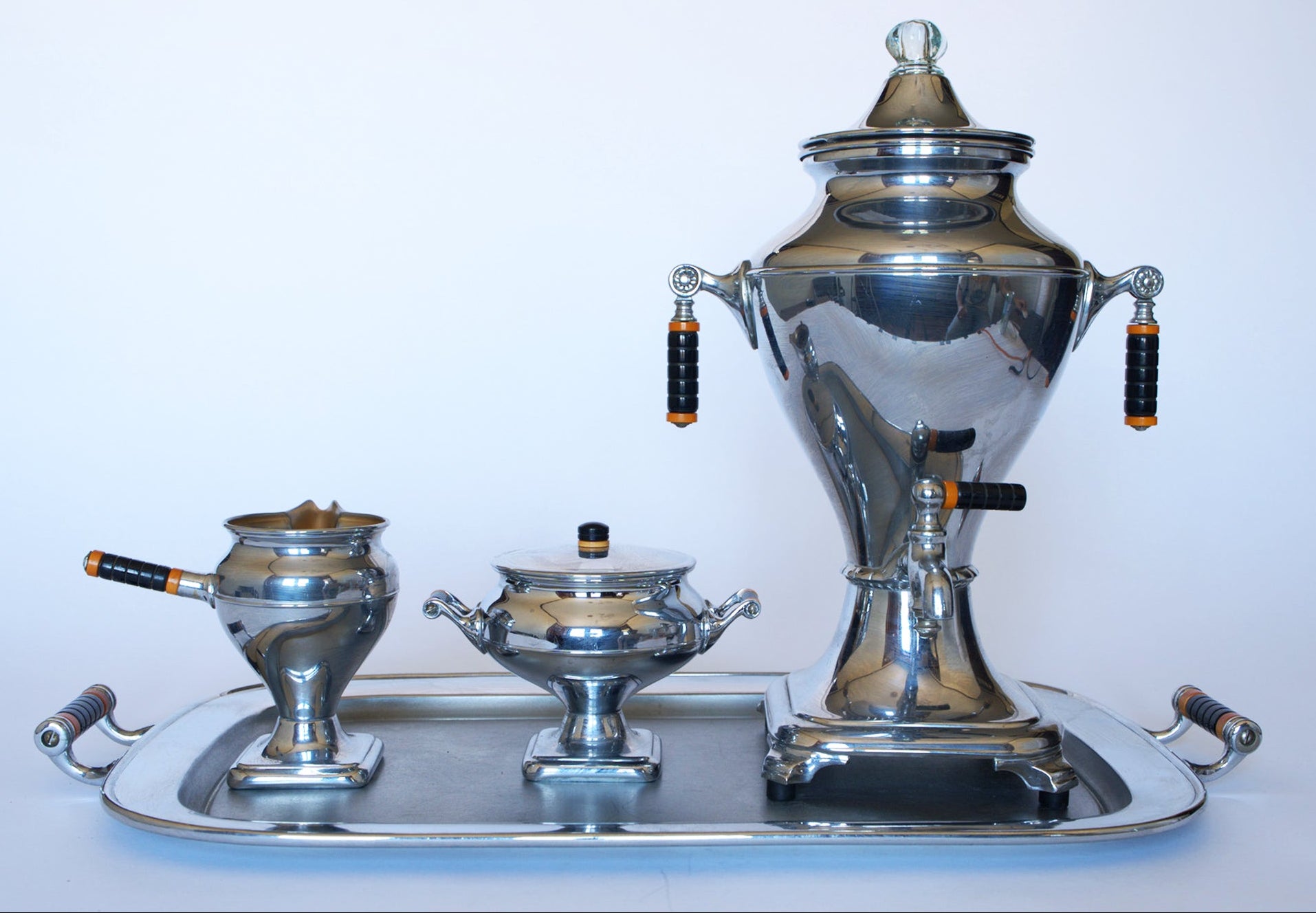 The Euro Trash Vintage Manning Bowman Chrome Coffee & Tea Service Set features a large urn, covered sugar bowl, and creamer with black and gold handles, all displayed on a tray against a plain white background.