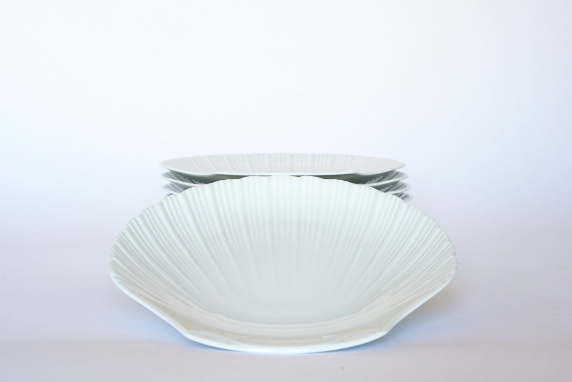 The Vintage White Ceramic Shell Plate Set by Euro Trash features five plates, with one upright and four stacked flat, adding coastal charm to your tableware against a plain white background.