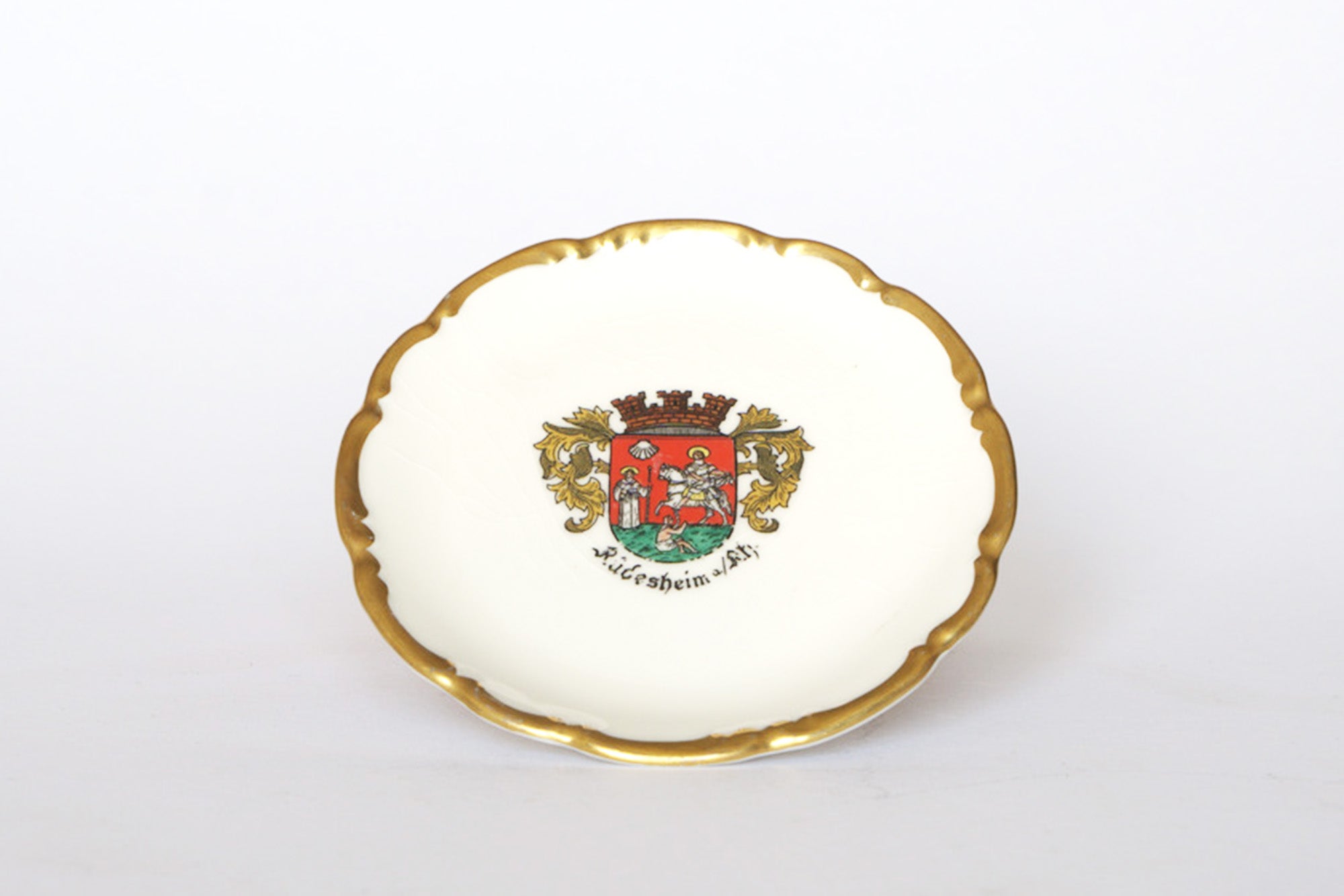 The Euro Trash Vintage Crest Porcelain Trinket Dish features a scalloped gold rim, colorful heraldic crest with two figures and gold lions, and is marked "Würzburg a/M. S.H.