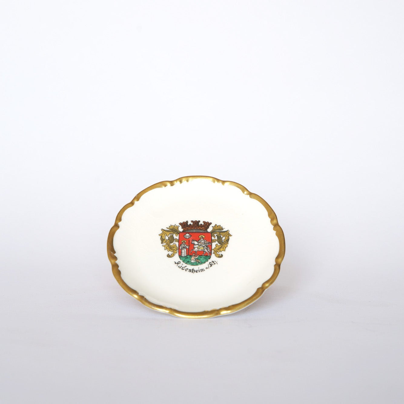 The Euro Trash Vintage Crest Porcelain Trinket Dish features a gold rim and a colorful heraldic crest with a red lion and shield. "Würzburg" is inscribed below, making this dish a charming addition to any collection.