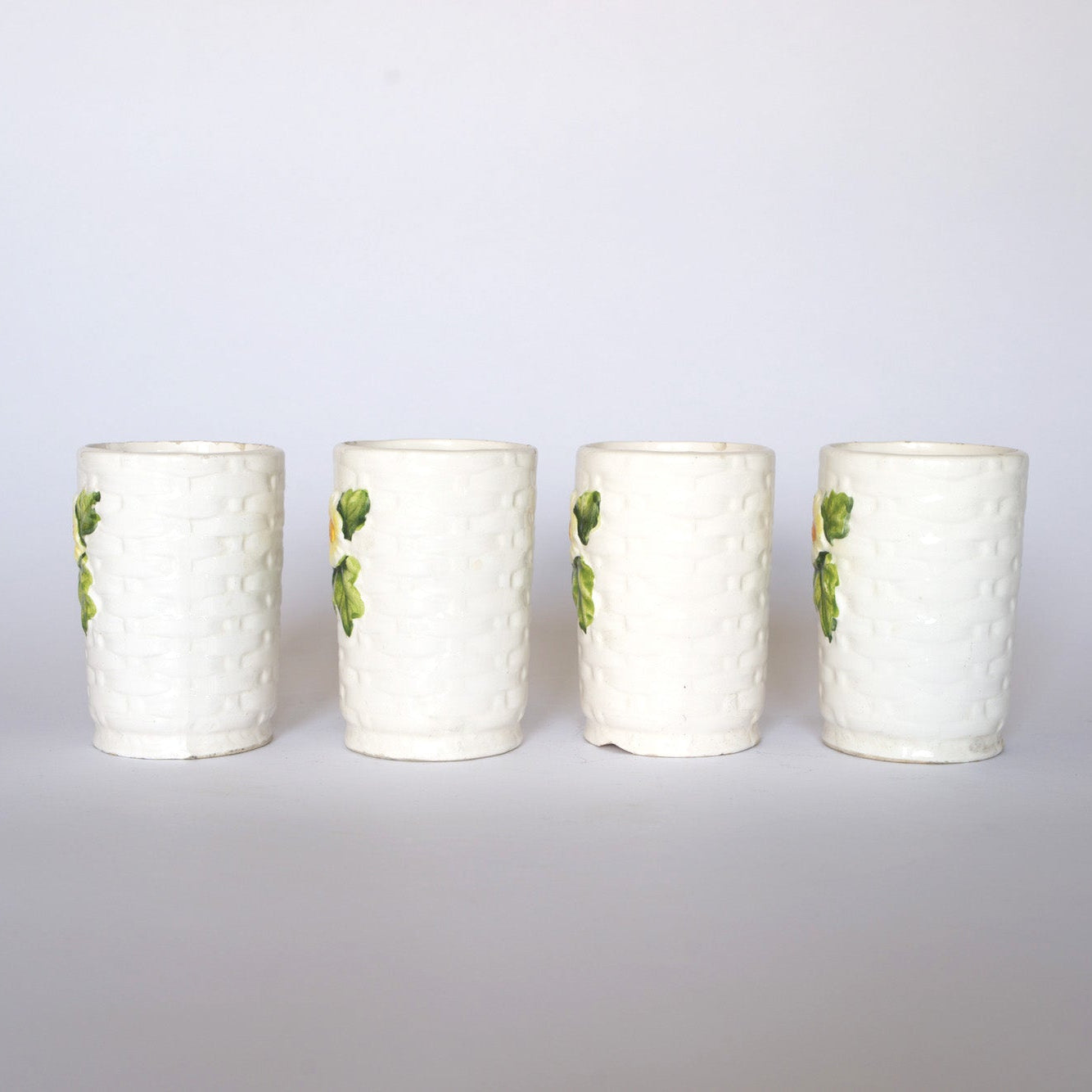 Four Vintage Ivy Motif Ceramic Bud Vases by Euro Trash, featuring a subtle woven texture and delicate green and yellow floral accents, are arranged side by side against a plain white background.