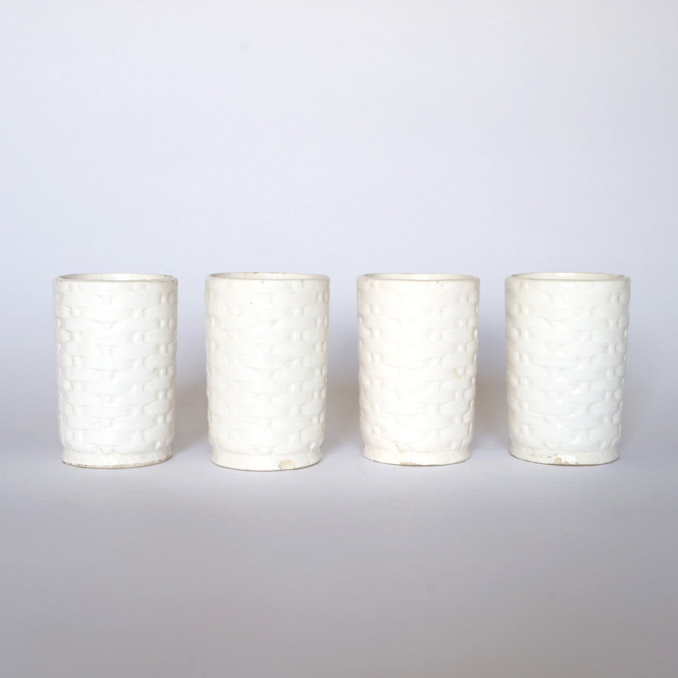 Four Euro Trash Vintage Ivy Motif Ceramic Bud Vases, featuring a white woven-like texture, are arranged in a straight line on a plain light background.