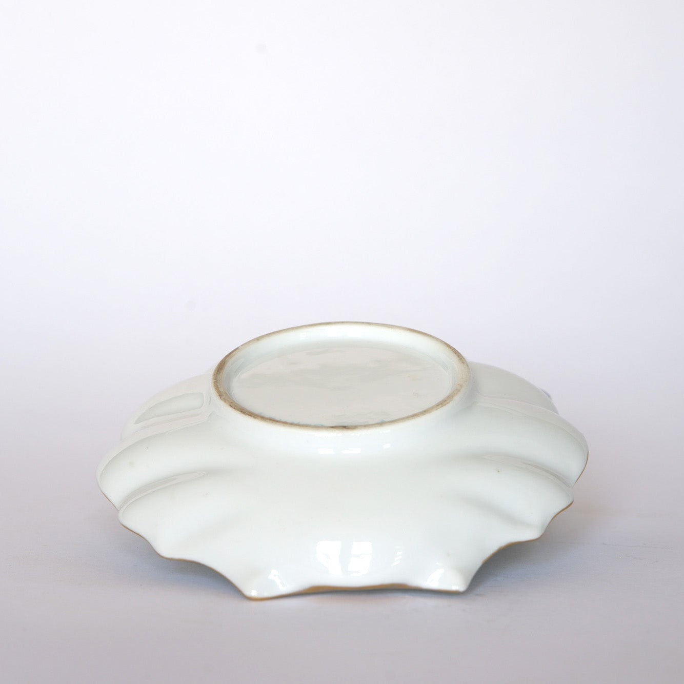 The Euro Trash Vintage Hand-Painted Floral Porcelain Plate with Gold Rim is displayed upside down on a white background, showing its flat, unglazed base and slightly raised rim.