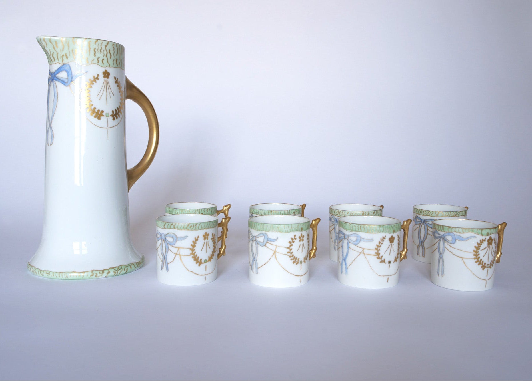The Euro Trash Vintage White Porcelain Teacup Set with Gold Handle features six teacups adorned with gold and blue wreath patterns, light green accents, and classic silhouettes on a crisp white background.