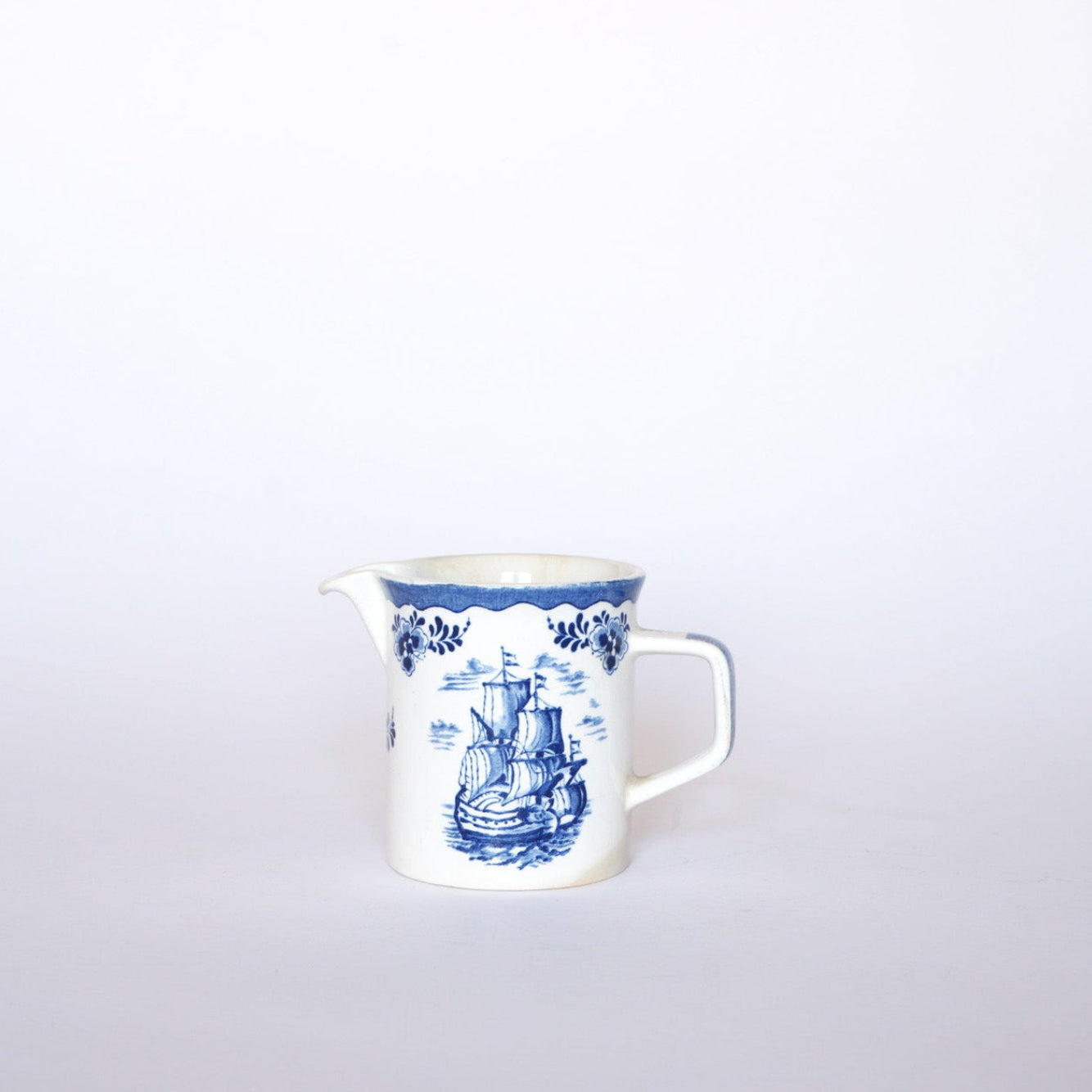 The Euro Trash Vintage Blue & White Ship Motif Porcelain Creamer features a nautical ship design on white porcelain with a blue floral border, offering a classic vintage feel.