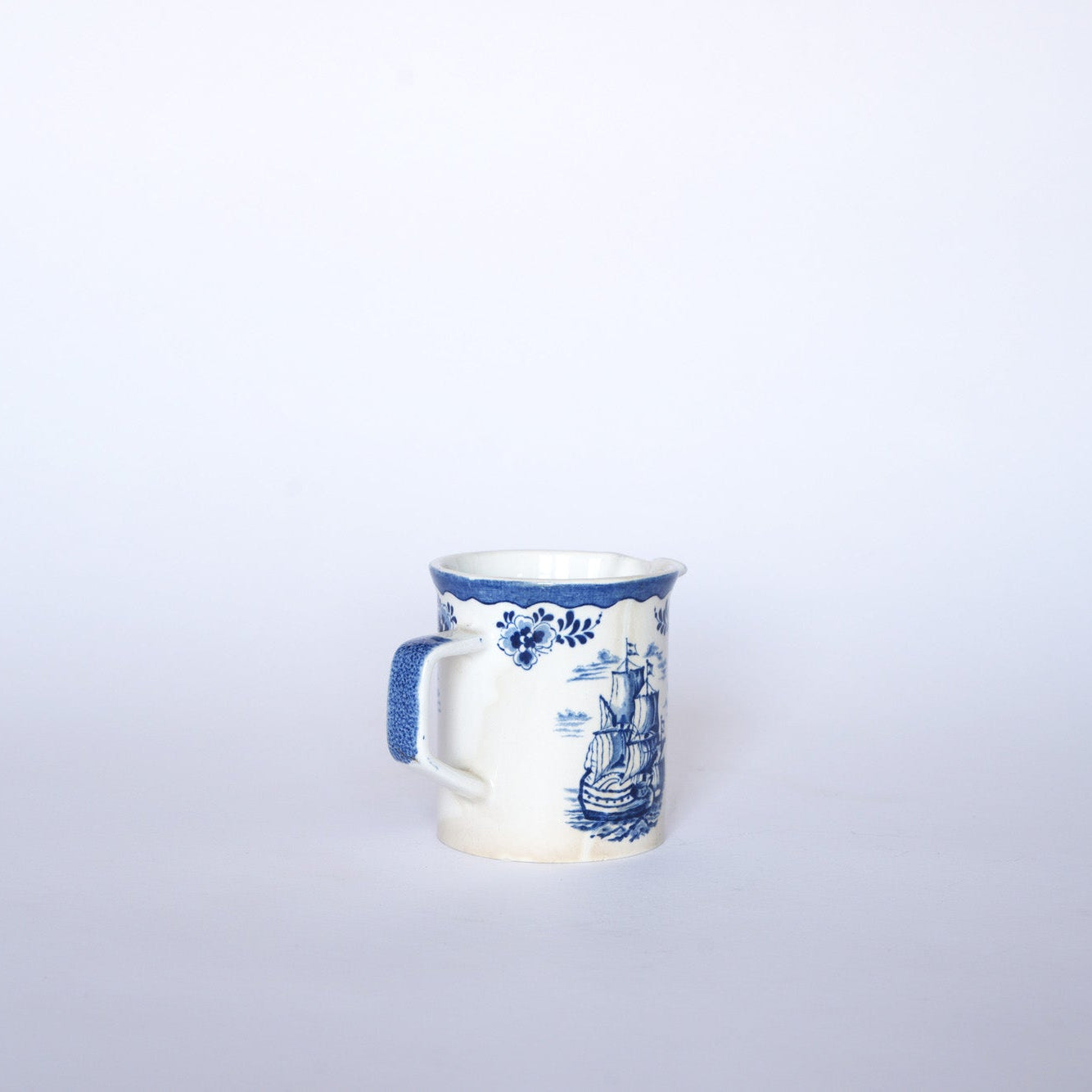 The Euro Trash Vintage Blue & White Ship Motif Porcelain Creamer features nautical and floral designs, with a blue handle, on a light background.