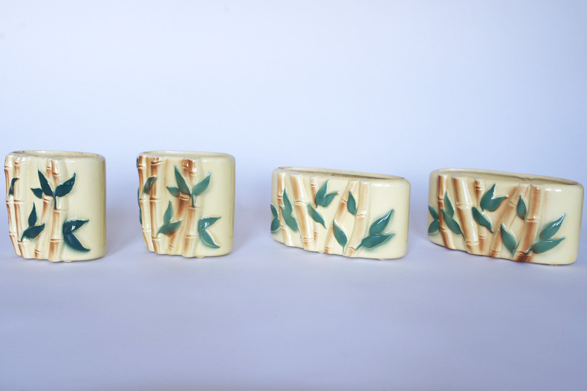 Four Euro Trash Vintage Bamboo Ceramic Vases, featuring a cream base with a green bamboo and leaf design, are displayed in a row against a plain light background.