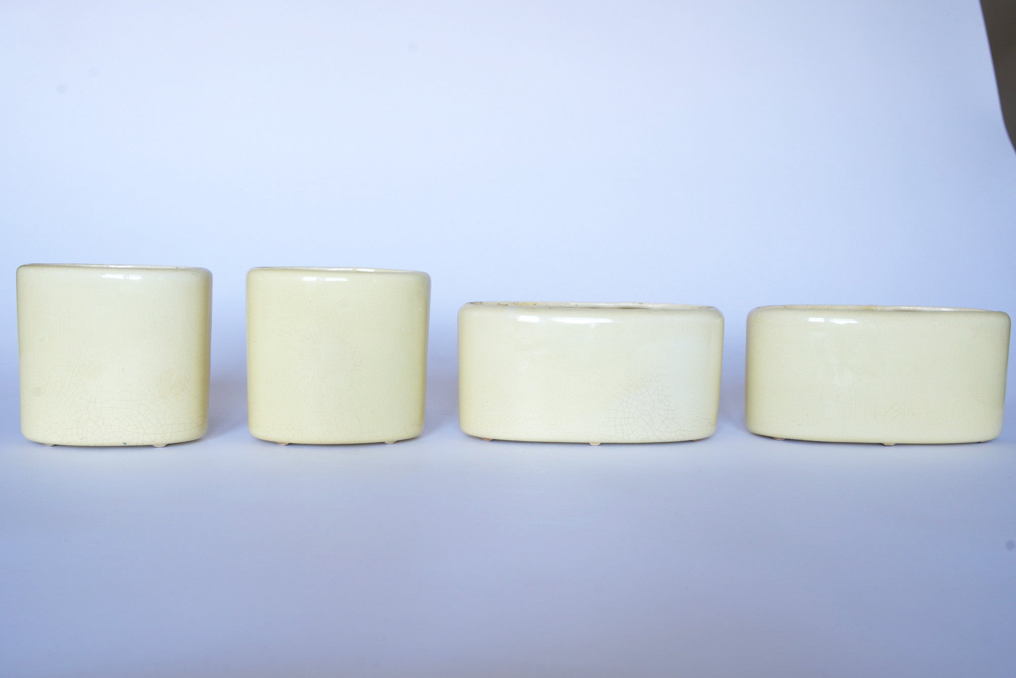 Four cream-colored Vintage Bamboo Ceramic Vases by Euro Trash, shaped as elegant cylinders, are arranged in a row against a plain white background.
