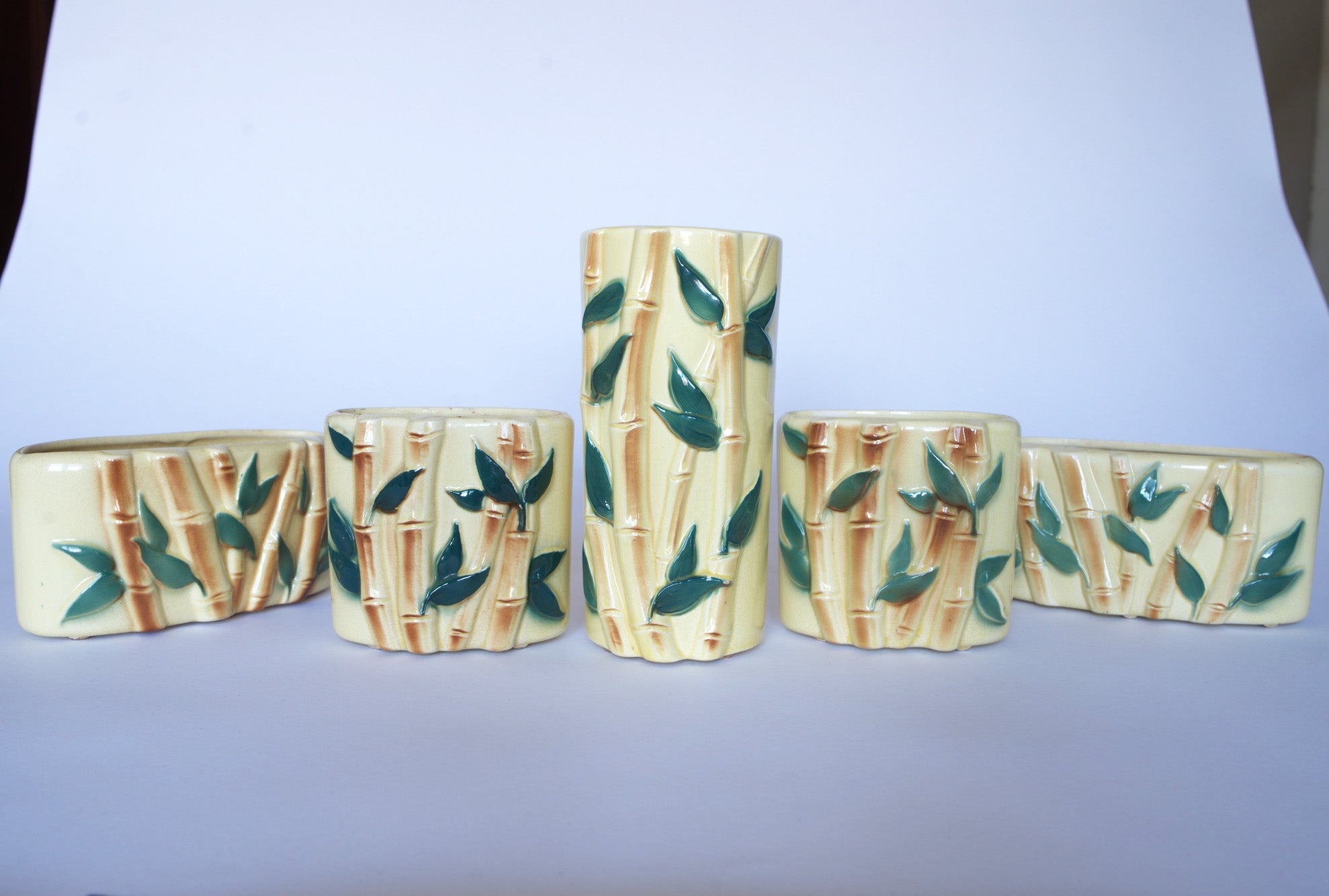 Five Vintage Bamboo Ceramic Vases by Euro Trash, featuring a bamboo and leaf design, are arranged in a row with the tallest vase at the center—ideal for adding nature-inspired style to your decor.