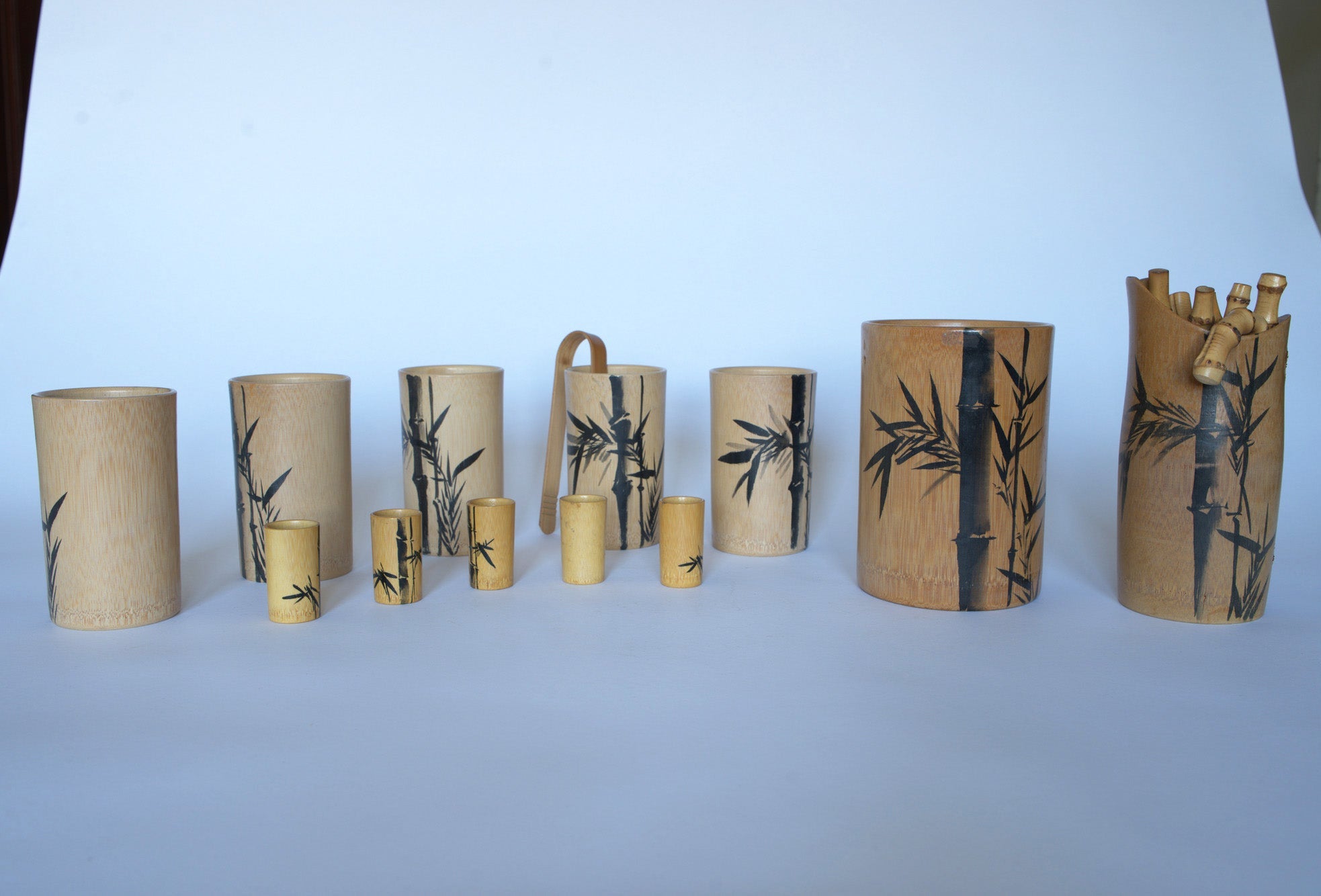 The Euro Trash Vintage Bamboo Motif Wooden Barware Set features cups, tumblers, and a jug with black bamboo designs, displayed on a white background—ideal for mid-century tropical decor.