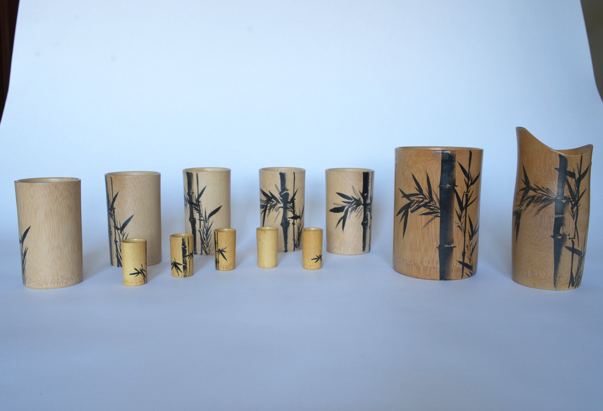 The Euro Trash Vintage Bamboo Motif Wooden Barware Set features bamboo cups and a black bamboo-accented pitcher, displayed on a white background—ideal for bringing mid-century tropical style to your entertaining space.