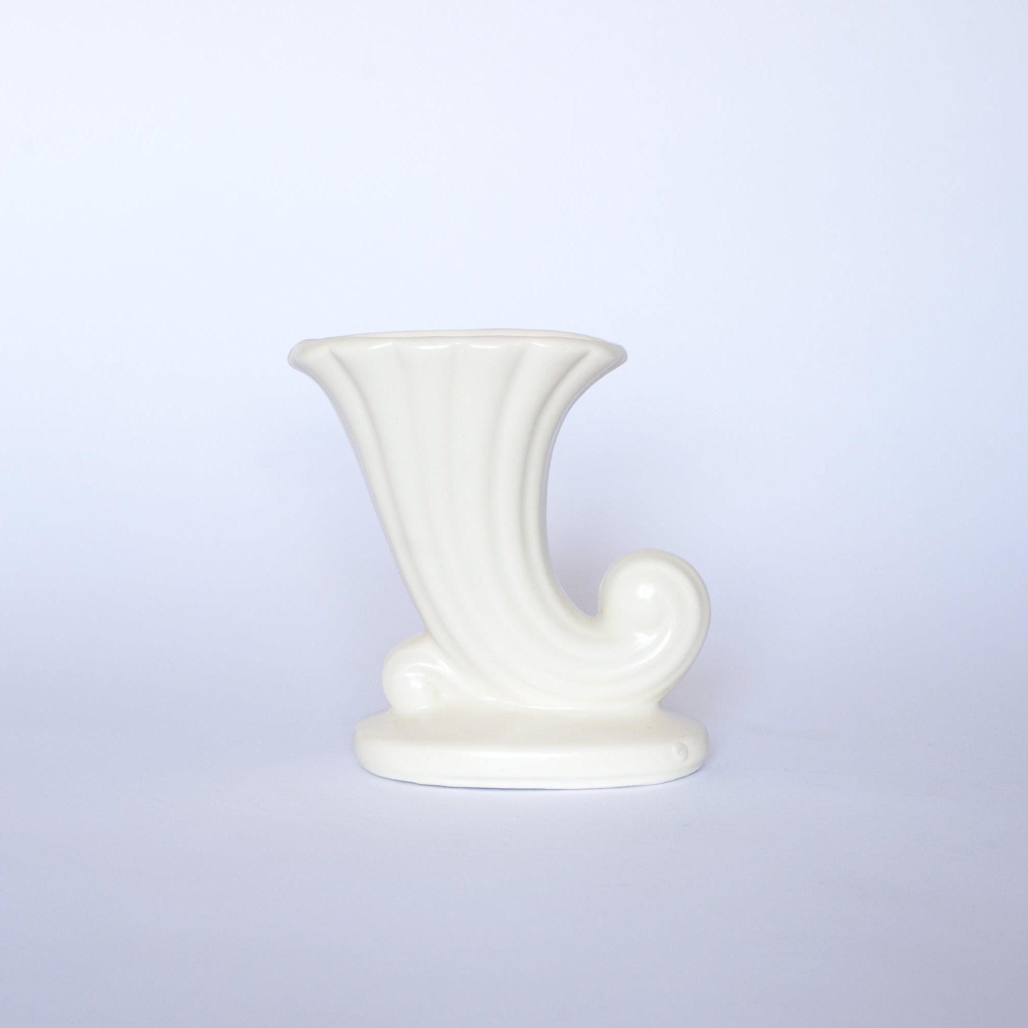 The Euro Trash Vintage White Cornucopia Ceramic Vase, with its horn shape and curled base, adds a charming decorative accent to any space.