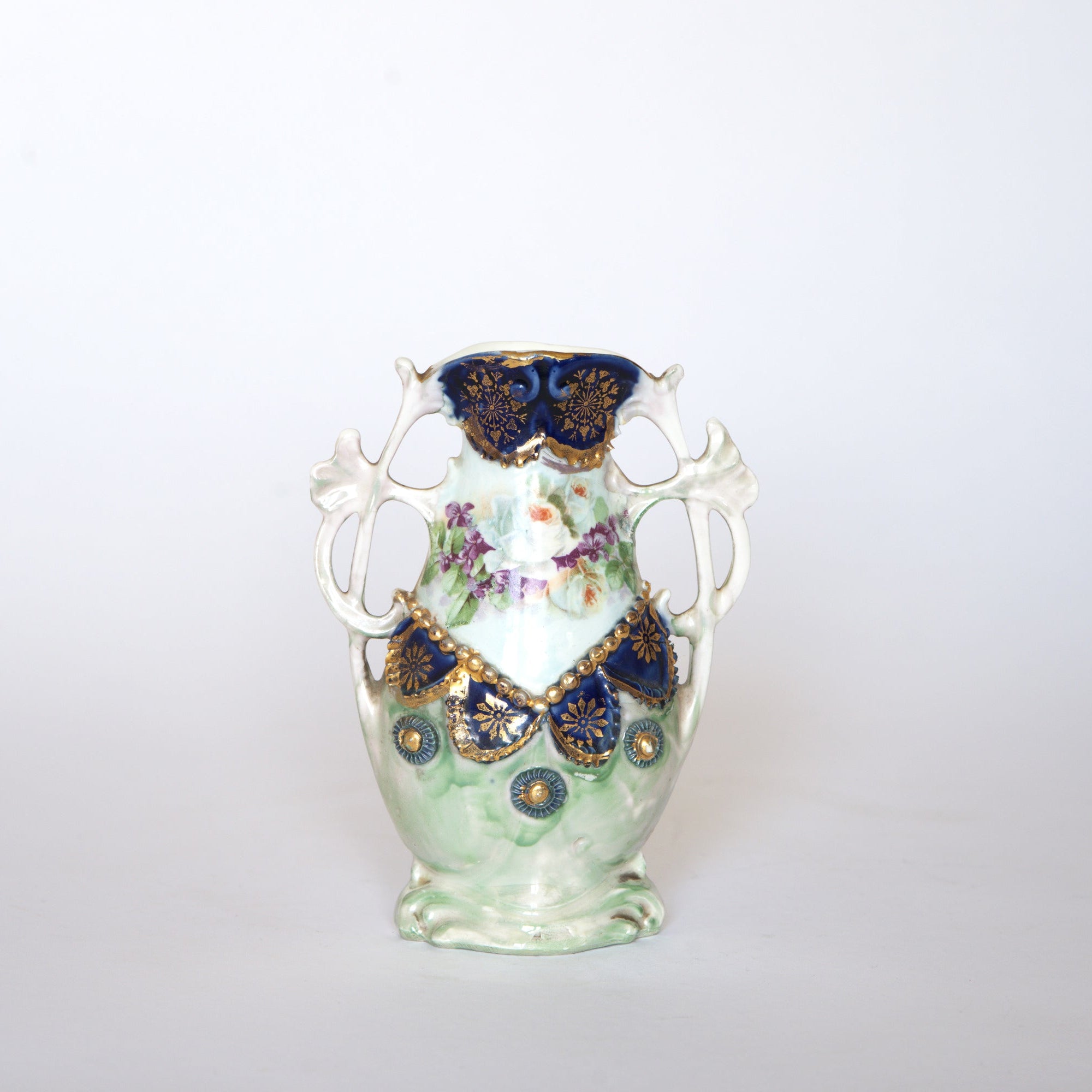 The Euro Trash Vintage Blue & Gold Porcelain Trinket Dish features a green and white body, cobalt blue and gold accents near the top, and a central floral design with soft purple and pink flowers on a plain white background.