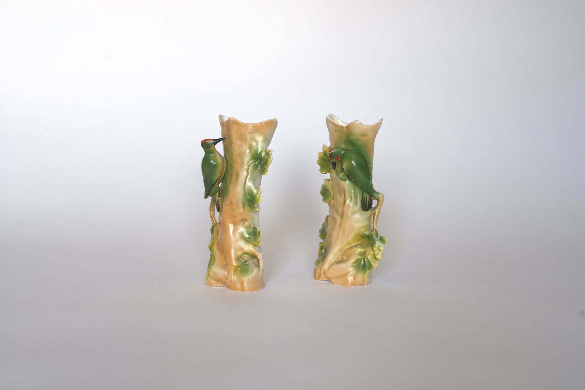 The Pair of Vintage Ceramic Hand-Painted Bird Vases by Euro Trash features tree trunk shapes with green leaves and perched birds, displayed side by side on a plain light background for a charming cottage look.