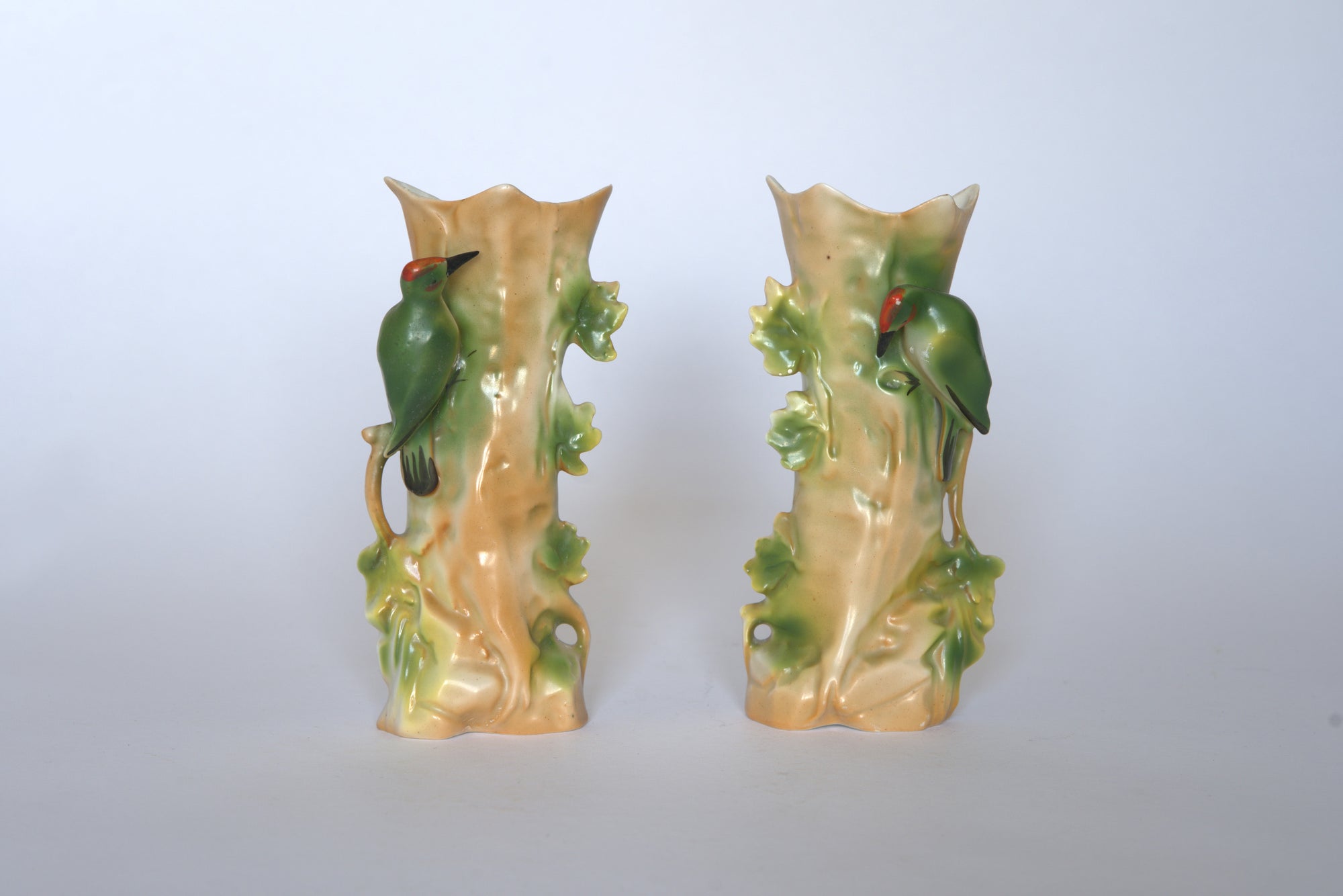 The Euro Trash Pair of Vintage Ceramic Hand-Painted Bird Vases features tree trunk shapes with green leaves and red-accented birds, all set against a plain white background for a charming cottage look.