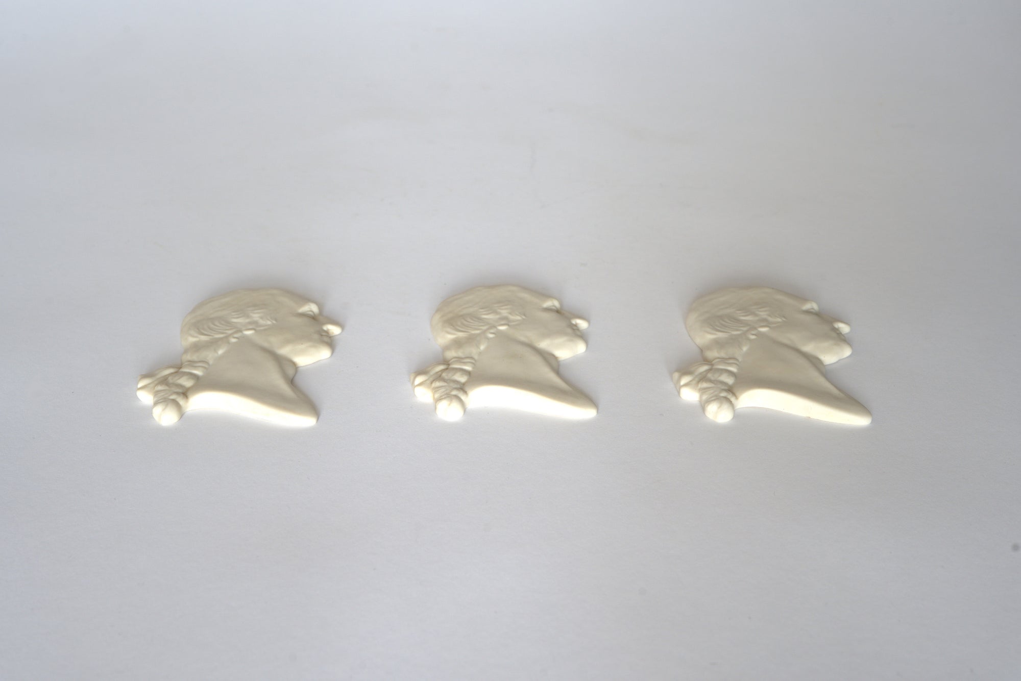 Three Vintage White Classical Bust Wall Plaques by Euro Trash, each facing left, are lined up on a plain light background, capturing the timeless elegance of neoclassical art.