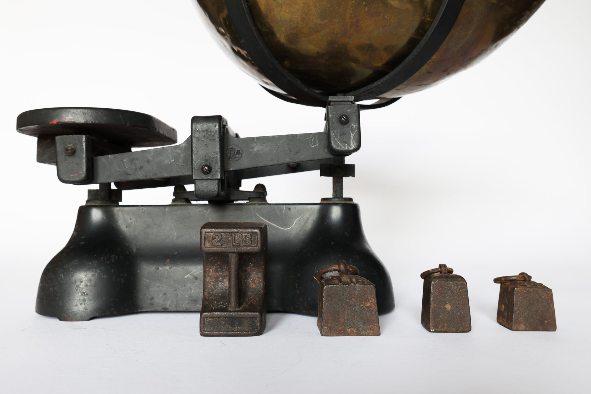The Euro Trash Annie Vintage Brass Balance Scale features a black finish, round left pan, and four metal weights (including a large 2-lb weight). This antique piece makes a striking decorative accent against a plain white background.