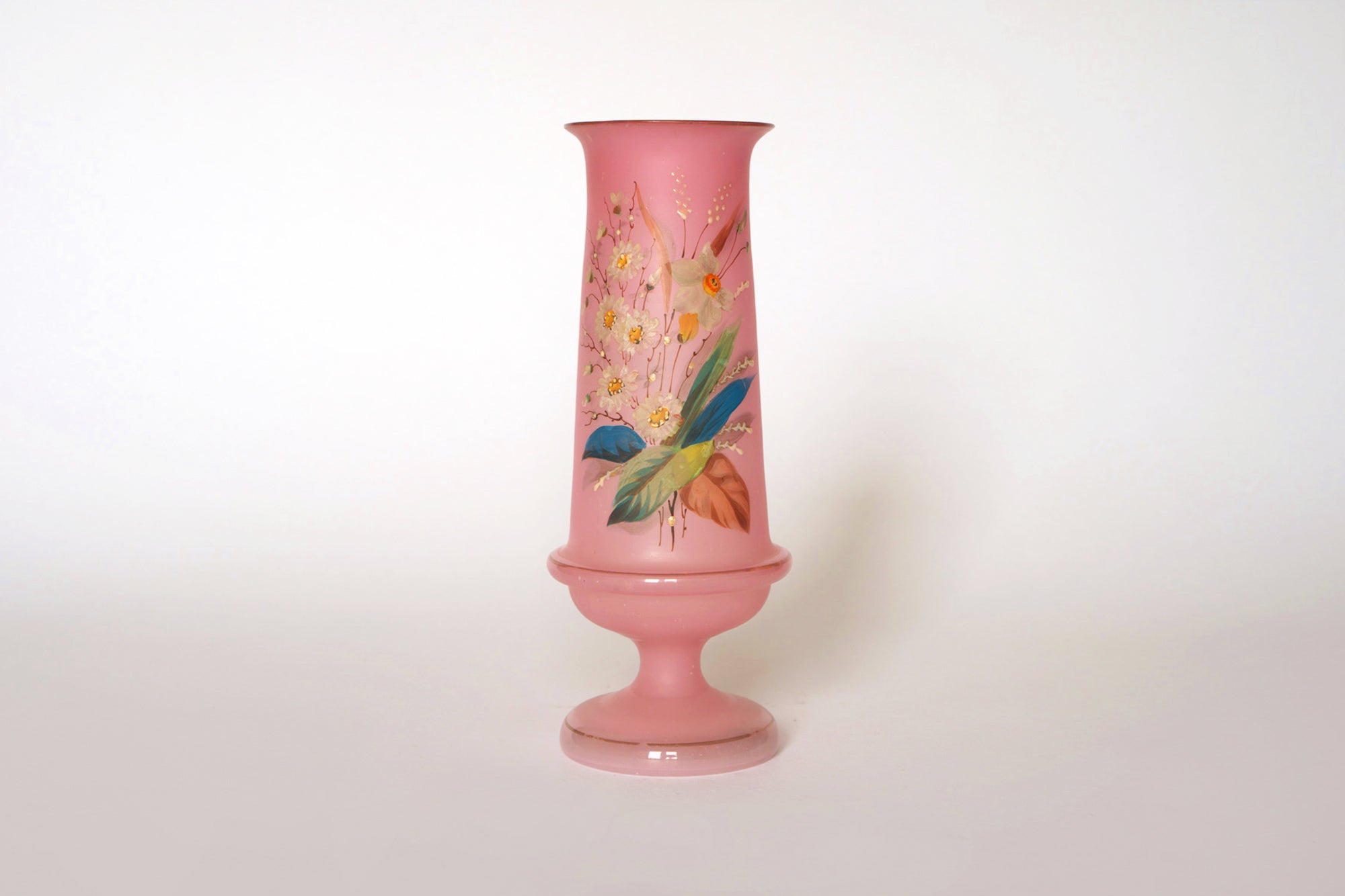 The Euro Trash Vintage Pink Floral Glass Vase features a tall, hand-painted design with colorful flowers and leaves on a white background, a wide base, and narrow neck for an elegant touch.