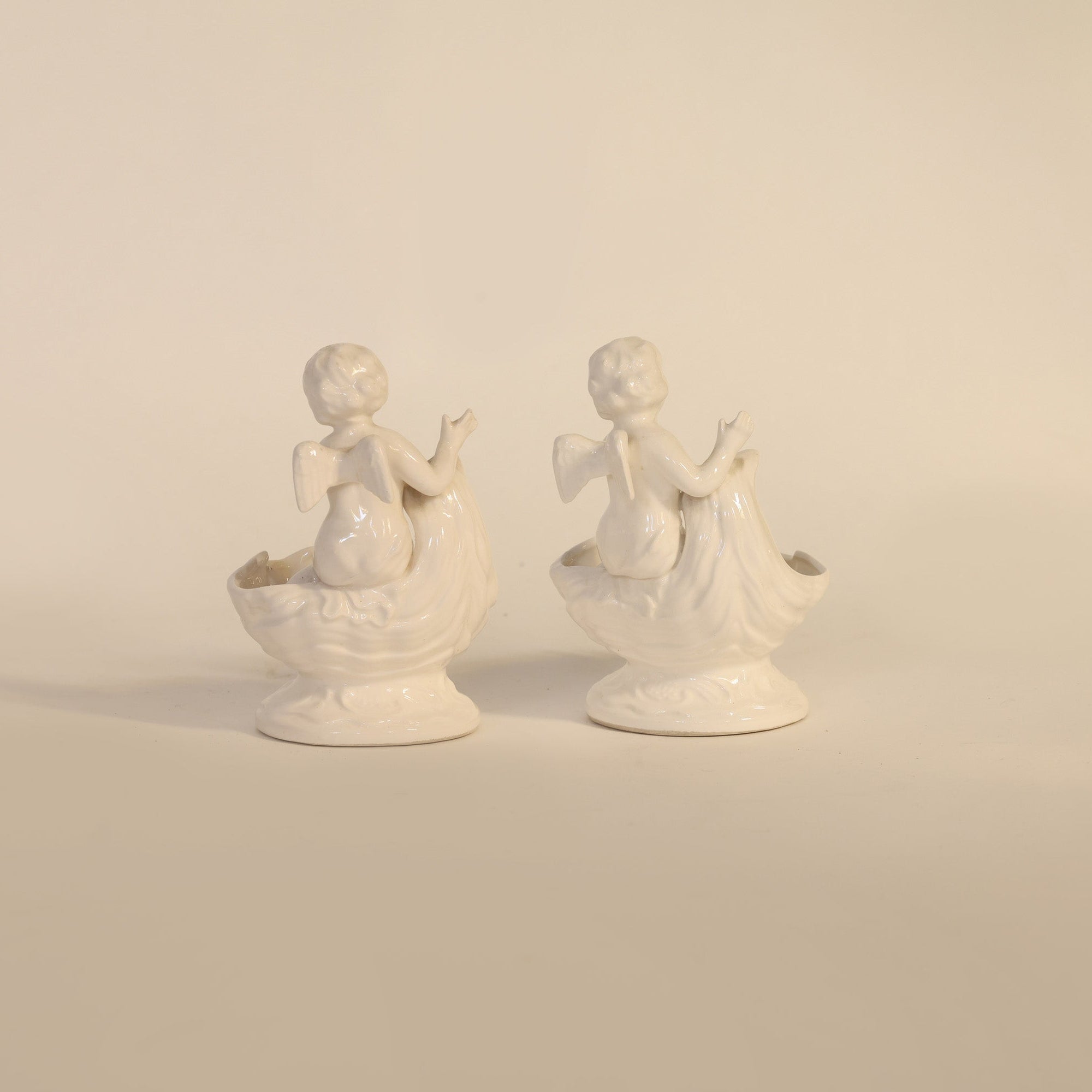 Two white ceramic cherub figures on a beige background