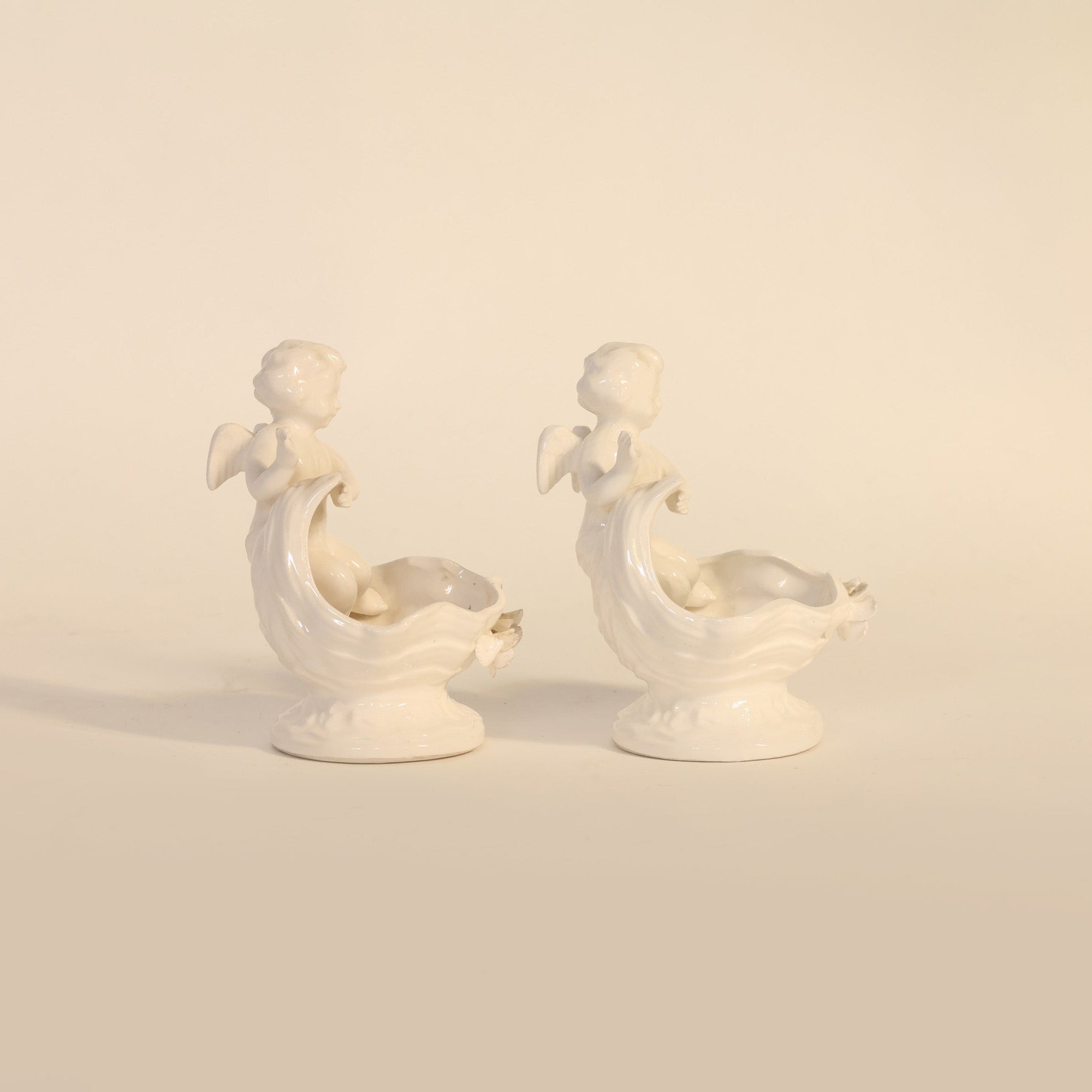 Two white ceramic cherub figures on a beige background