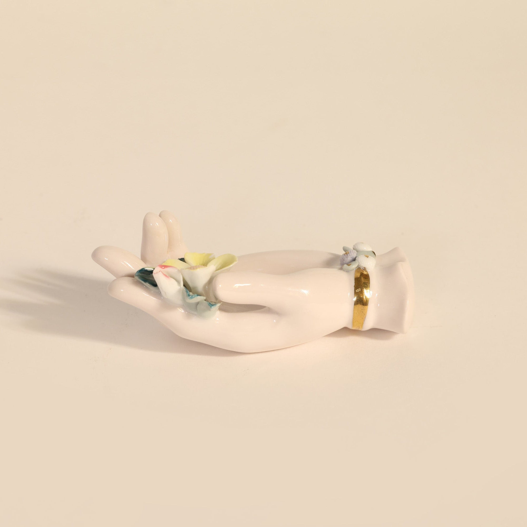 White ceramic hand holding a flower on a beige background