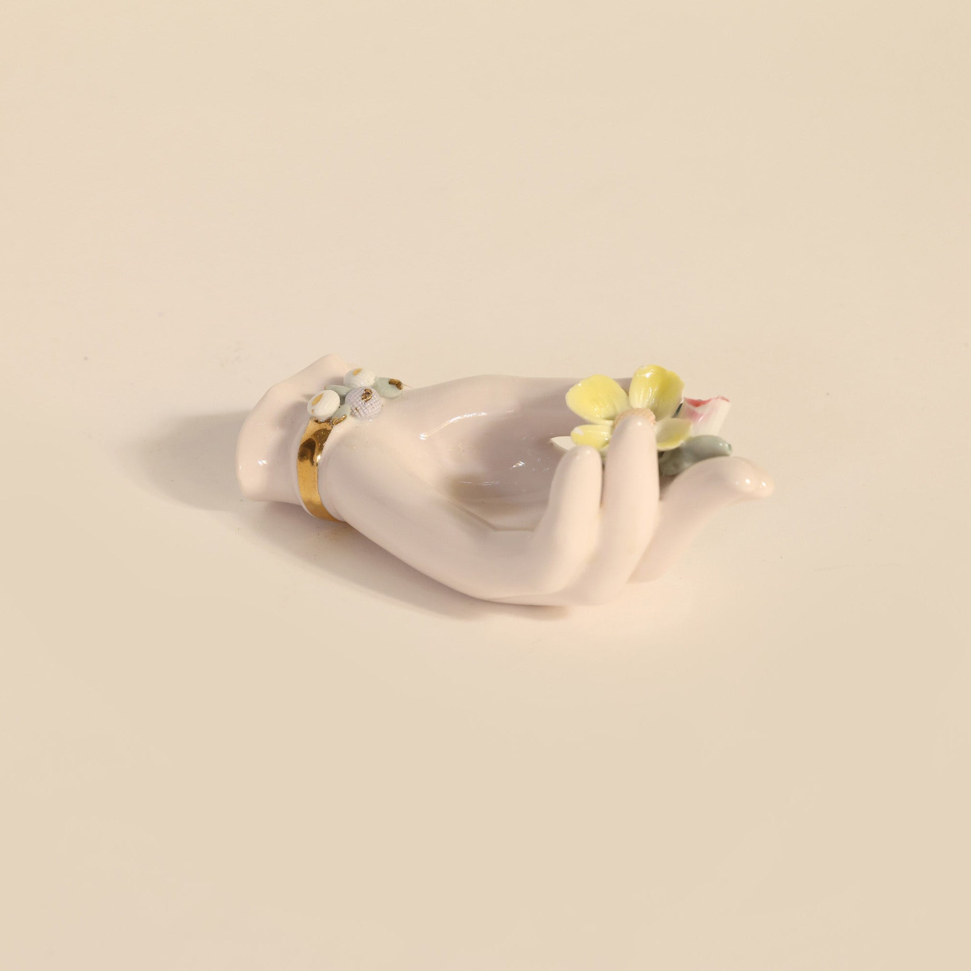 White ceramic hand figurine with a small flower on a beige background