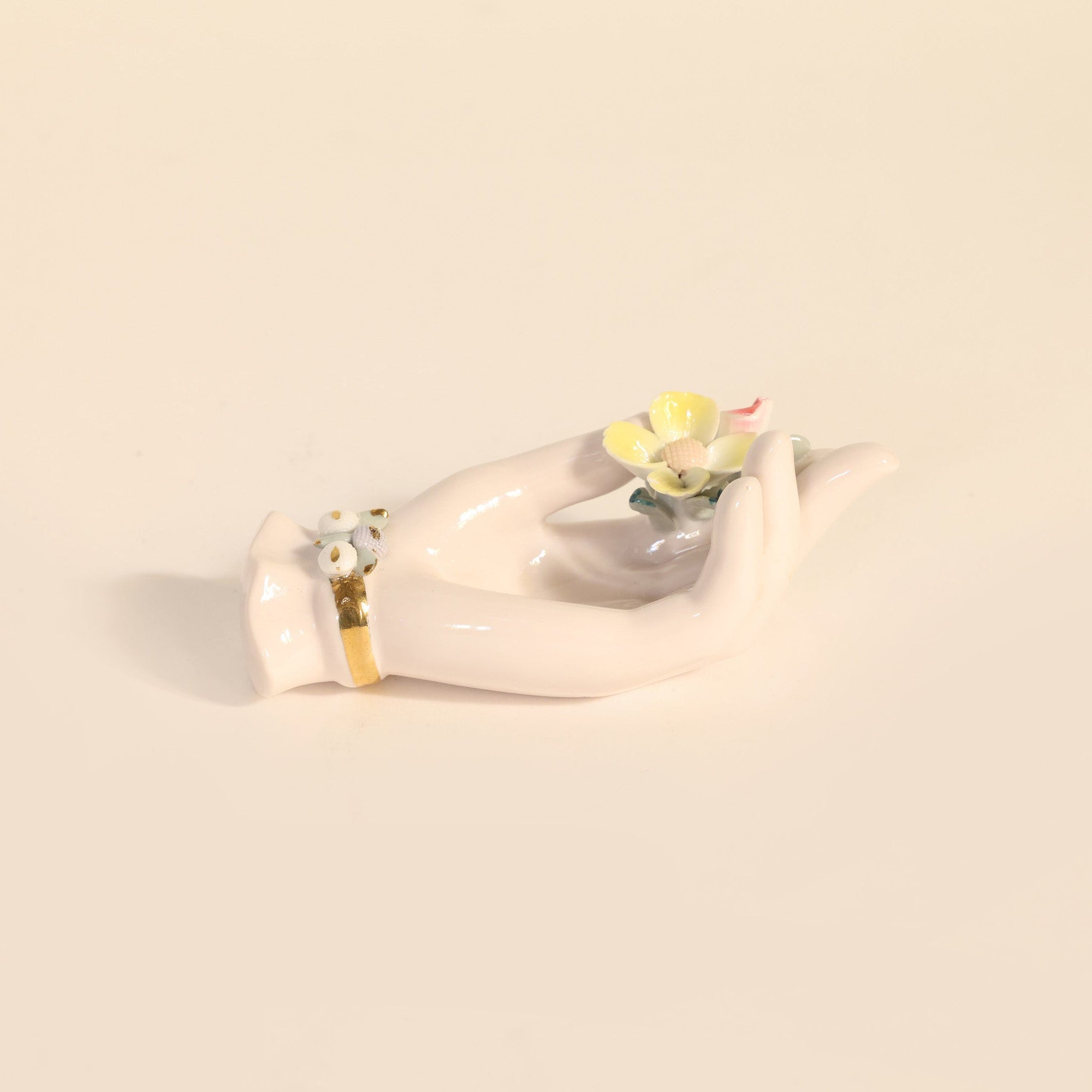White ceramic hand holding a small flower on a beige background.