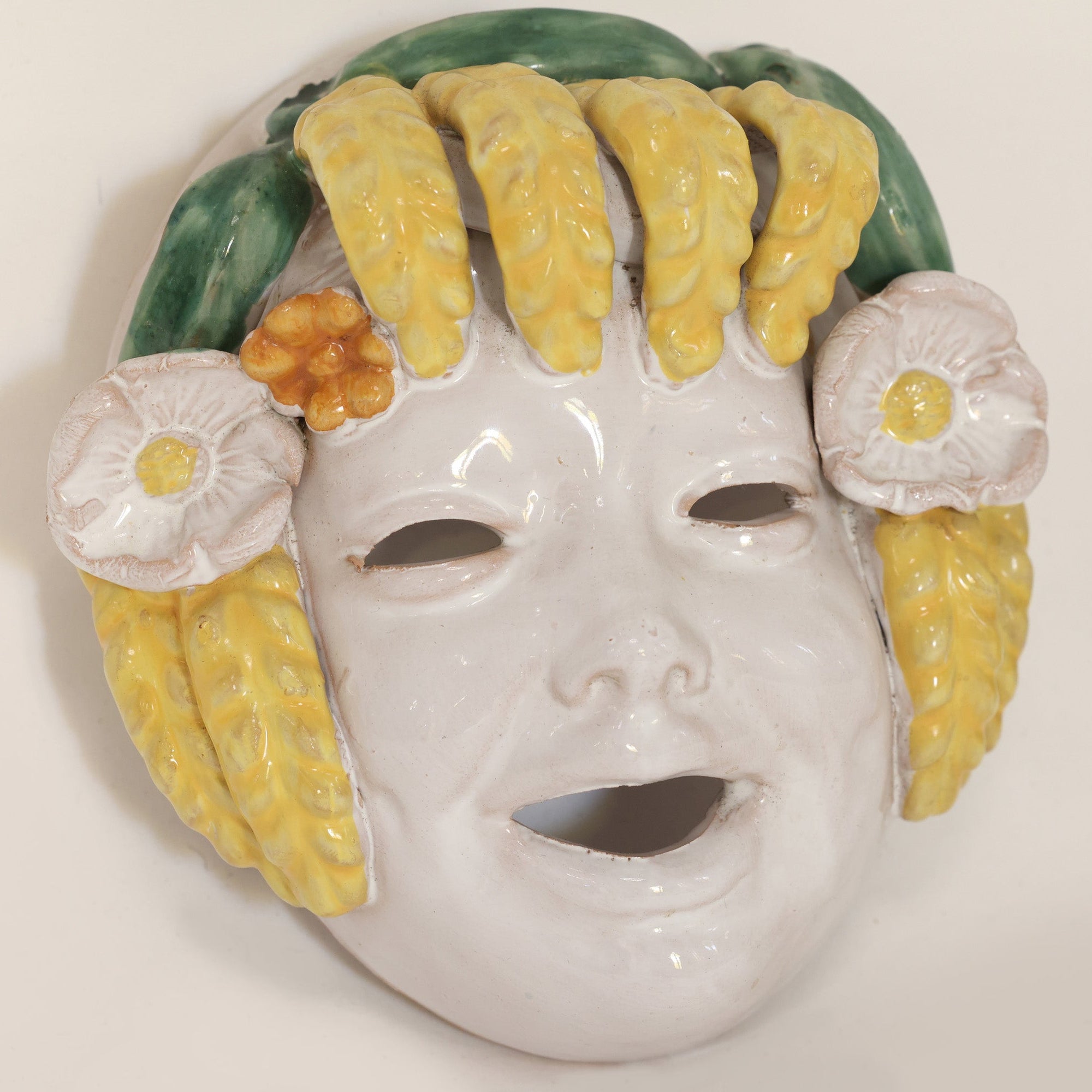 Decorative mask with yellow hair and floral accessories on a beige background