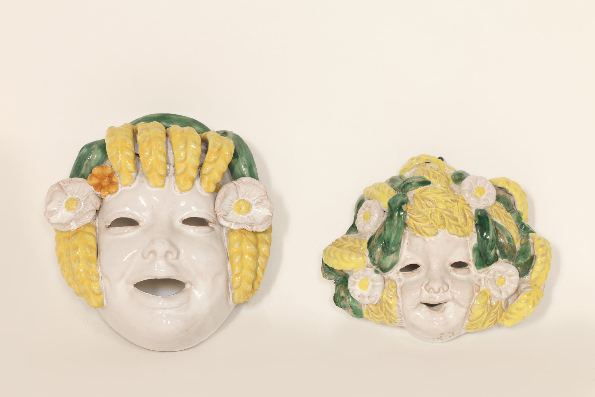 Pair of Italian majolica wall masks with floral design on beige background