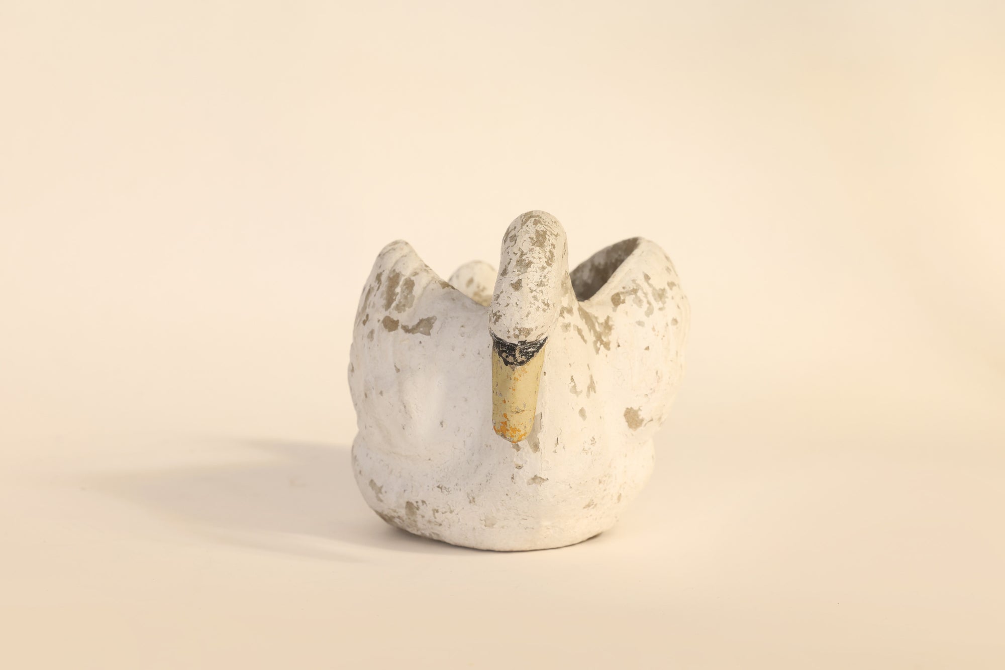 Ceramic swan-shaped object on a beige background
