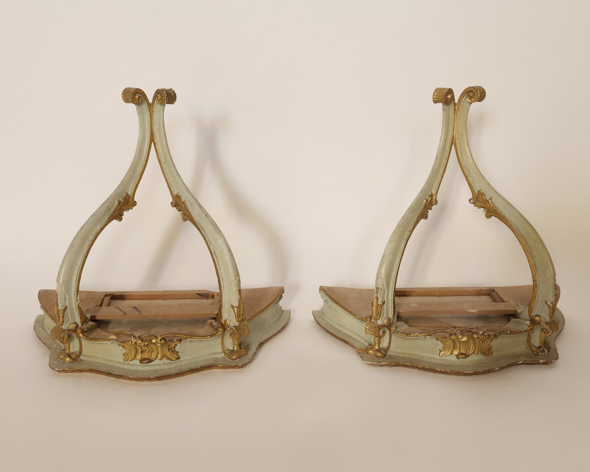 A Pair Of Vintage Giltwood Wall Corbels by Euro Trash Annie, featuring ornate curved legs and gold accents reminiscent of antique decor, are displayed side by side without seats, exposing their internal structure against a plain background.
