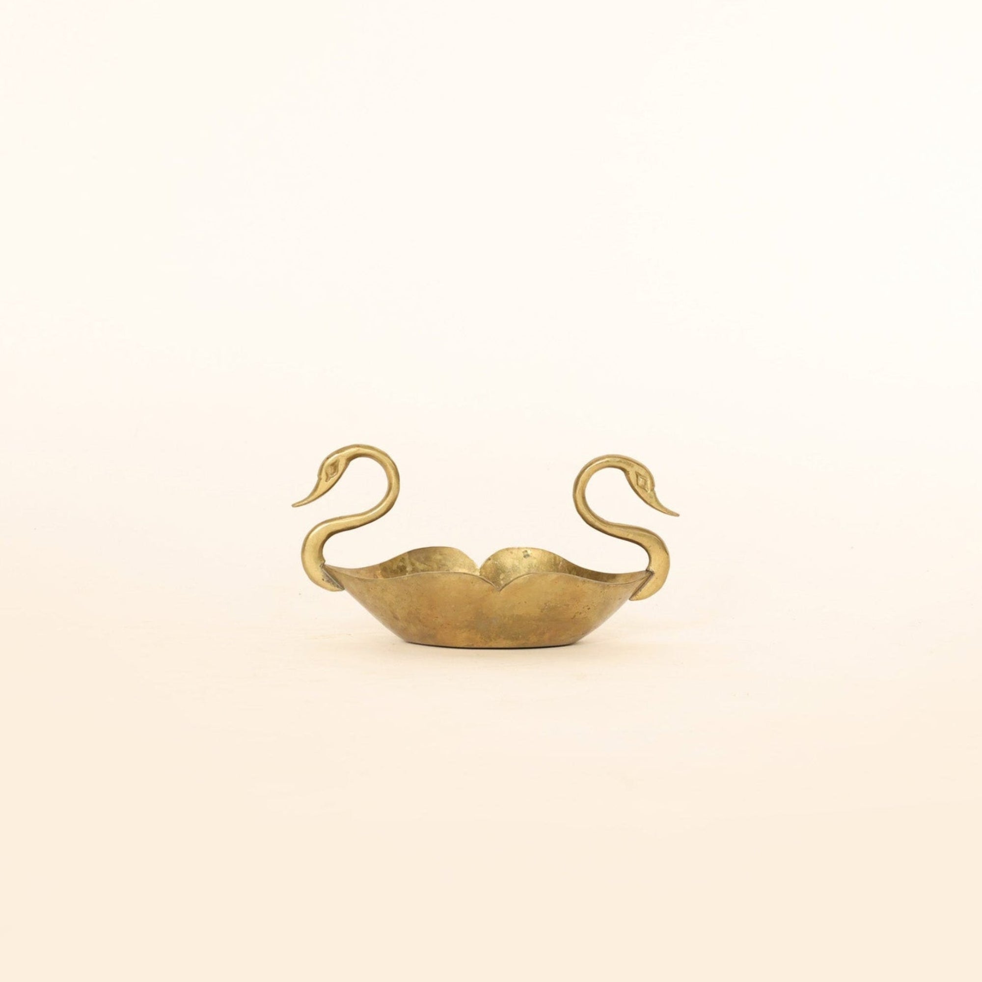 Gold swan-shaped object on a beige background